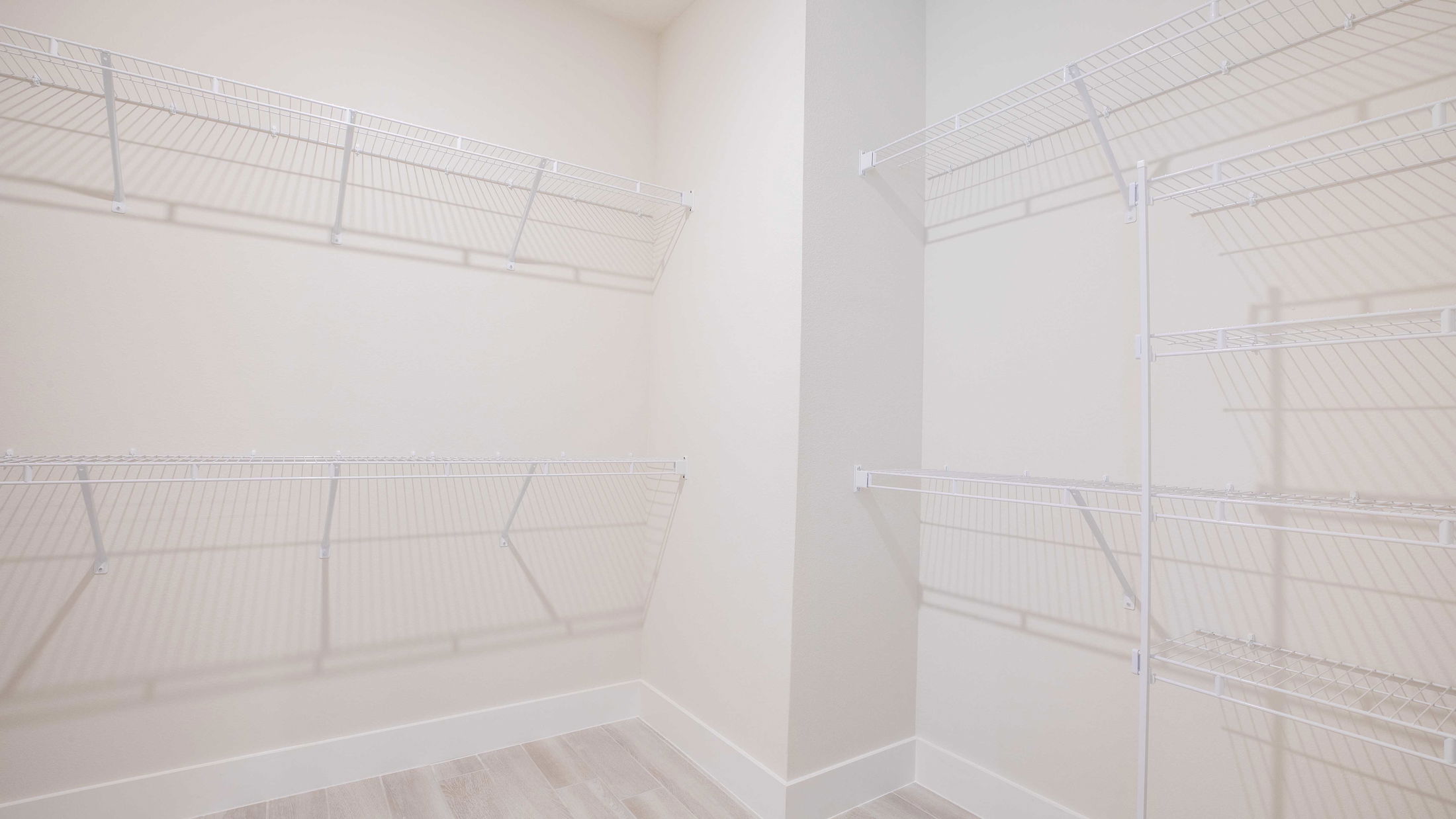 Spacious walk-in closet with white wire shelving and light wood flooring.