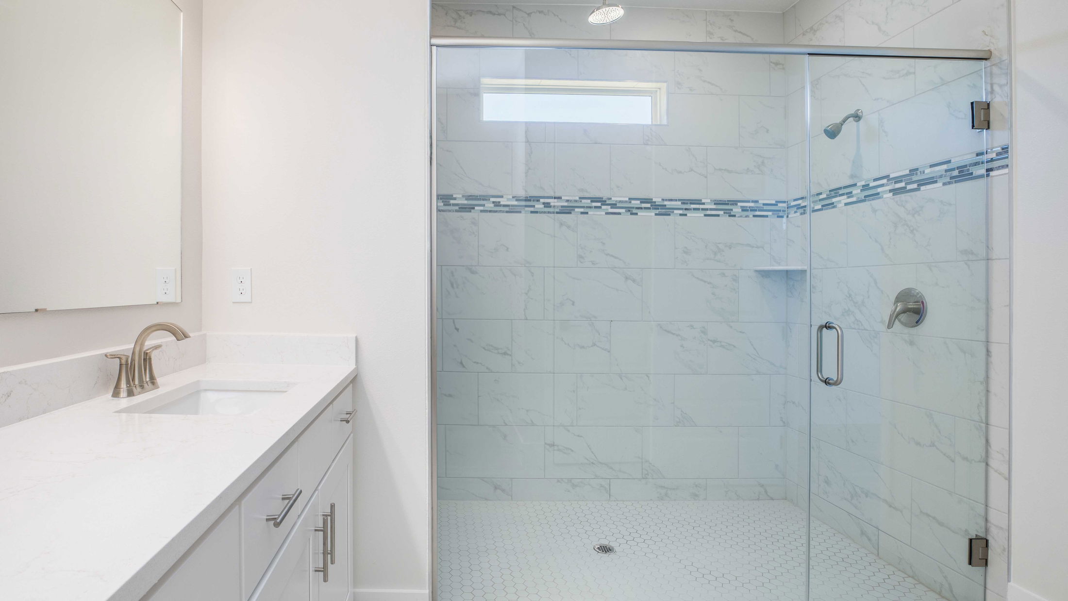 Modern bathroom with a glass-enclosed marble-tiled shower and white vanity with brushed nickel fixtures.