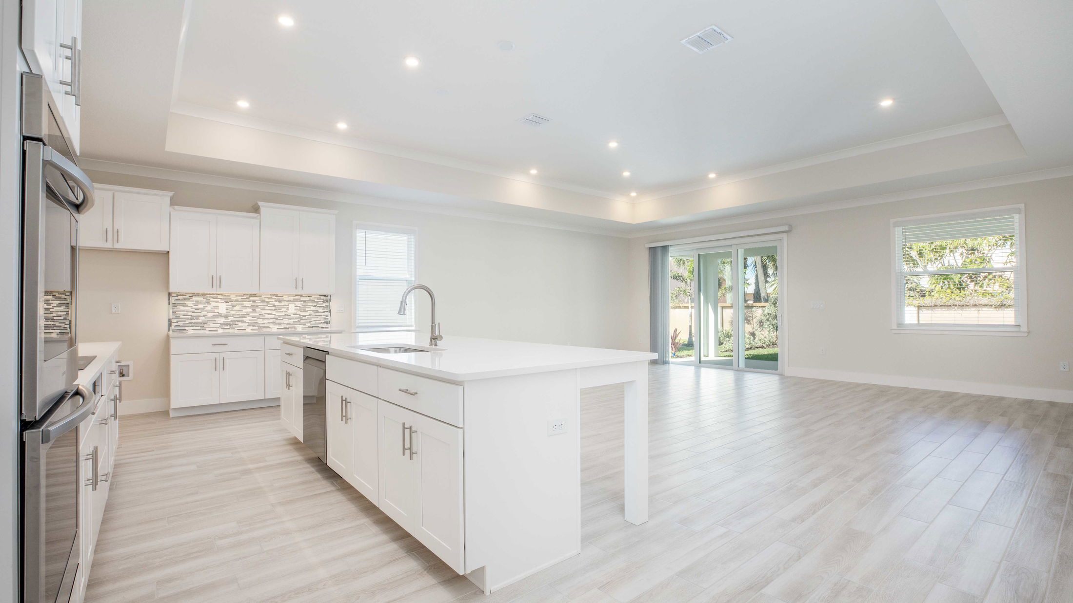 Modern open-concept kitchen and living area with white cabinets, island, and sliding glass doors leading to a garden.