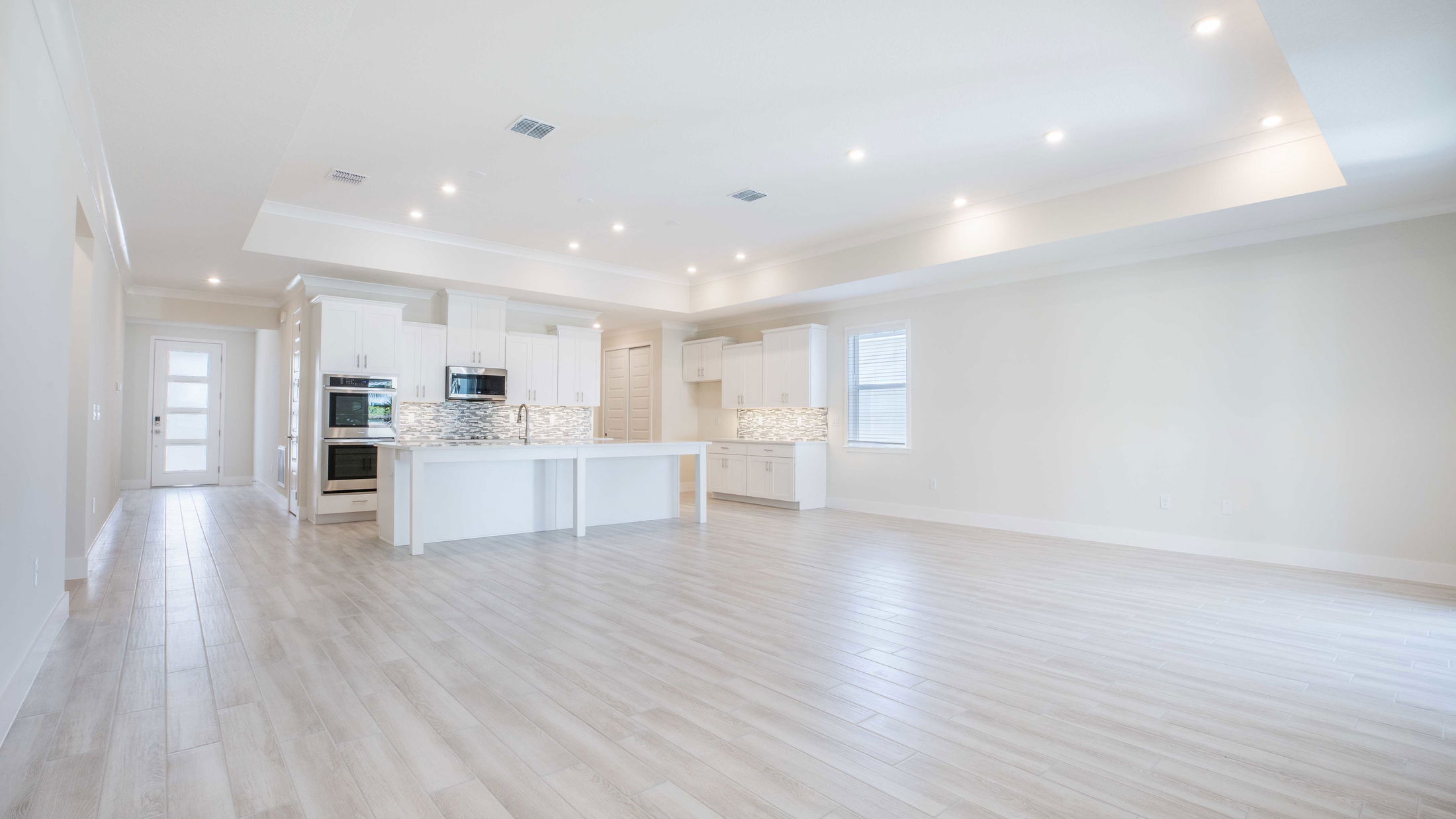 Modern open-concept kitchen with white cabinets, island, and light wood flooring illuminated by recessed lights.