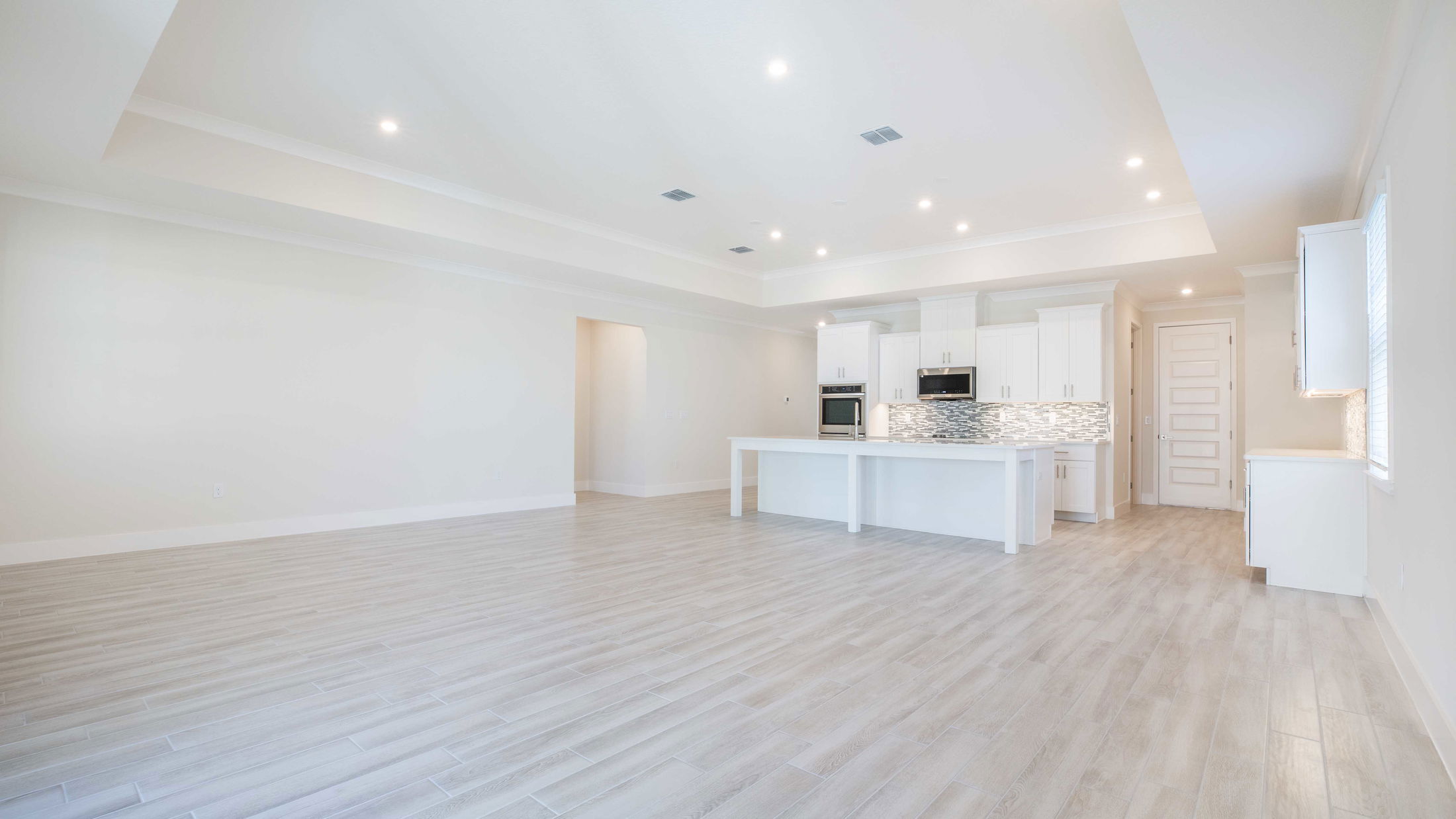 Spacious modern kitchen with white cabinets, island, and tiled backsplash in an open-concept layout.