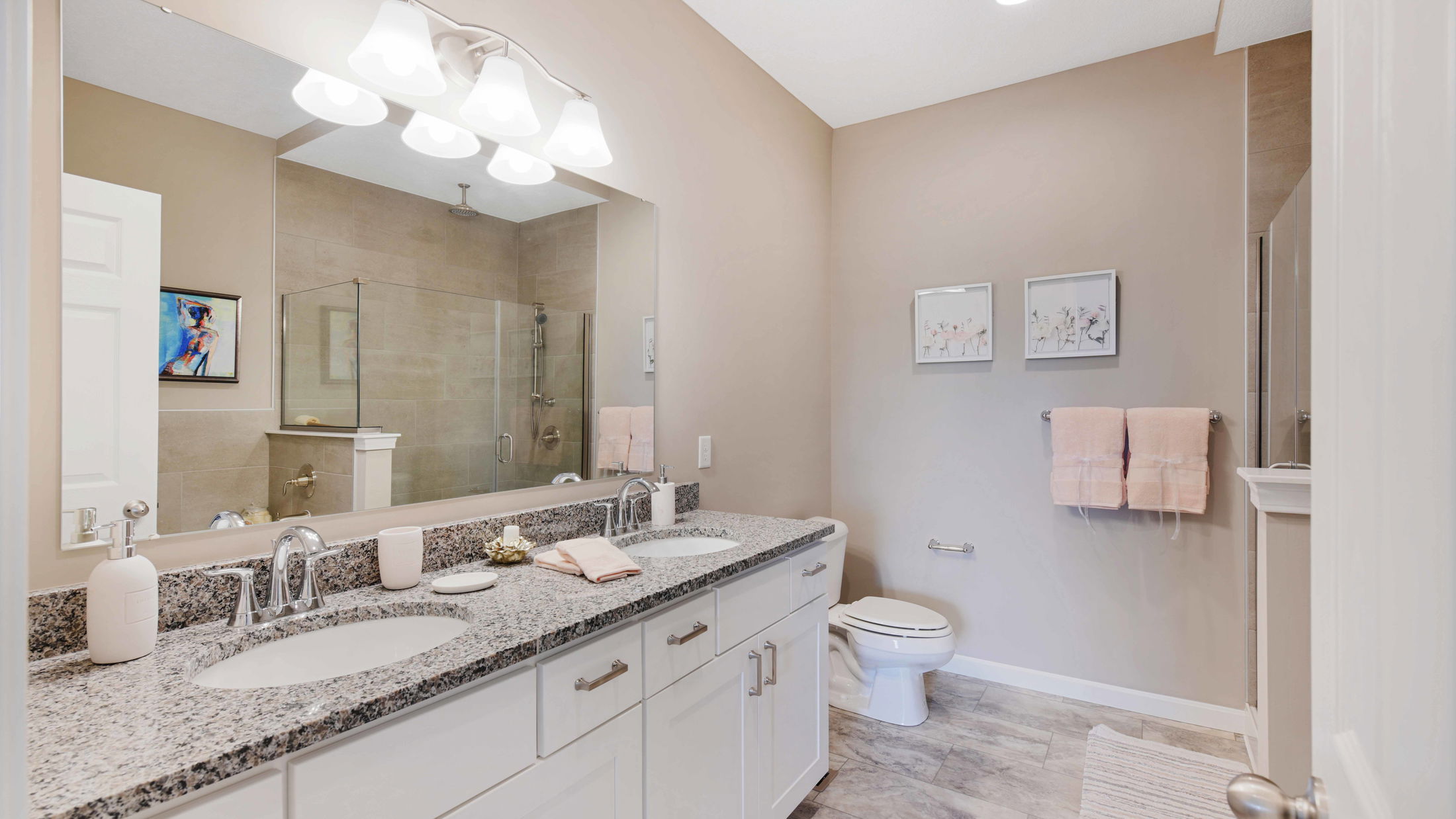 Modern bathroom with granite countertops, double sinks, large mirror, glass-enclosed shower, and beige walls.