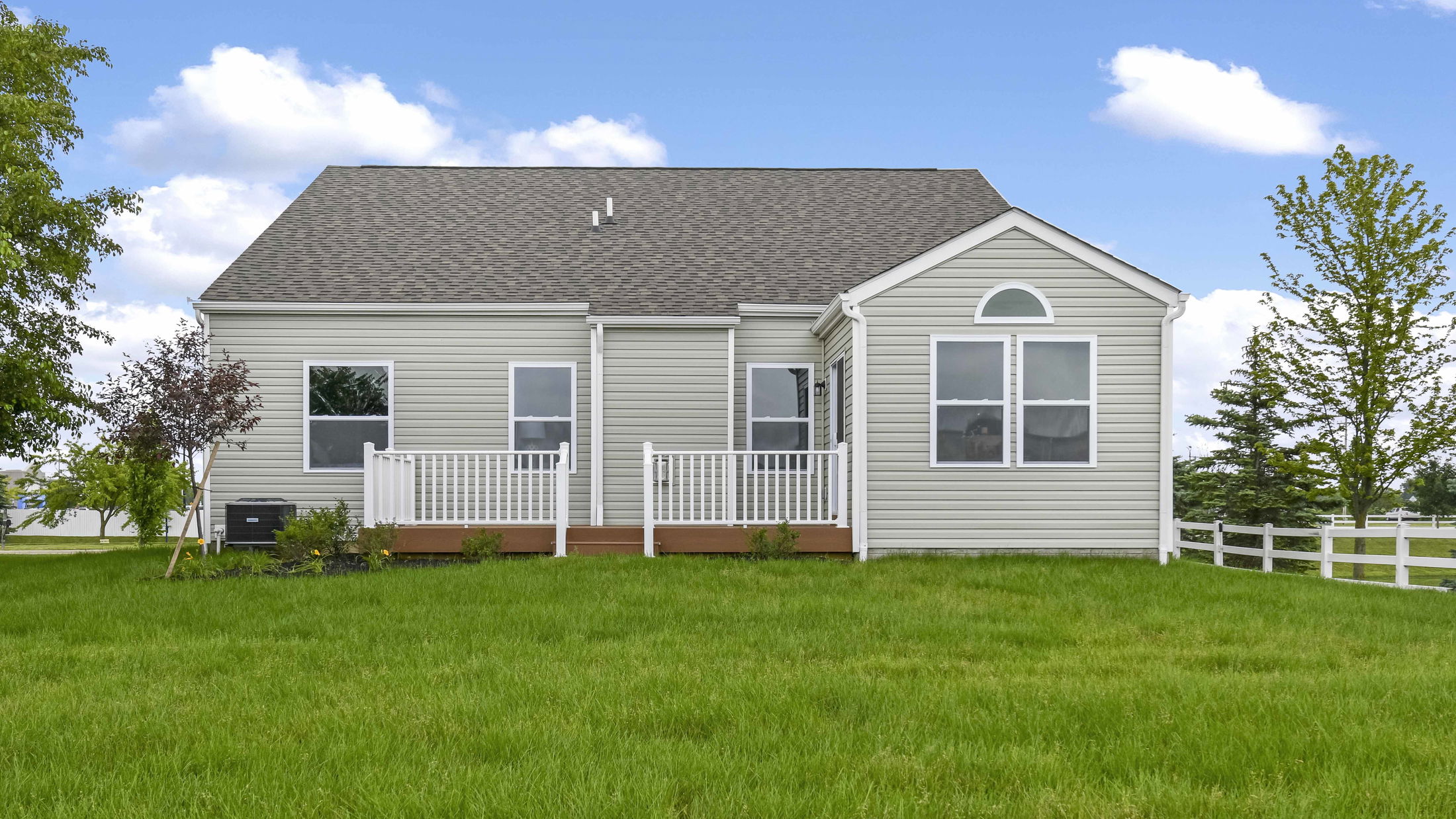 Single-story gray house with white trim and a spacious green lawn under a clear blue sky.