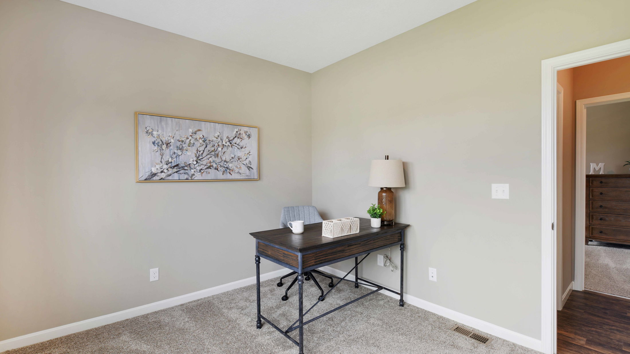 A minimalist home office with a dark wooden desk, chair, lamp, wall art, and neutral decor.