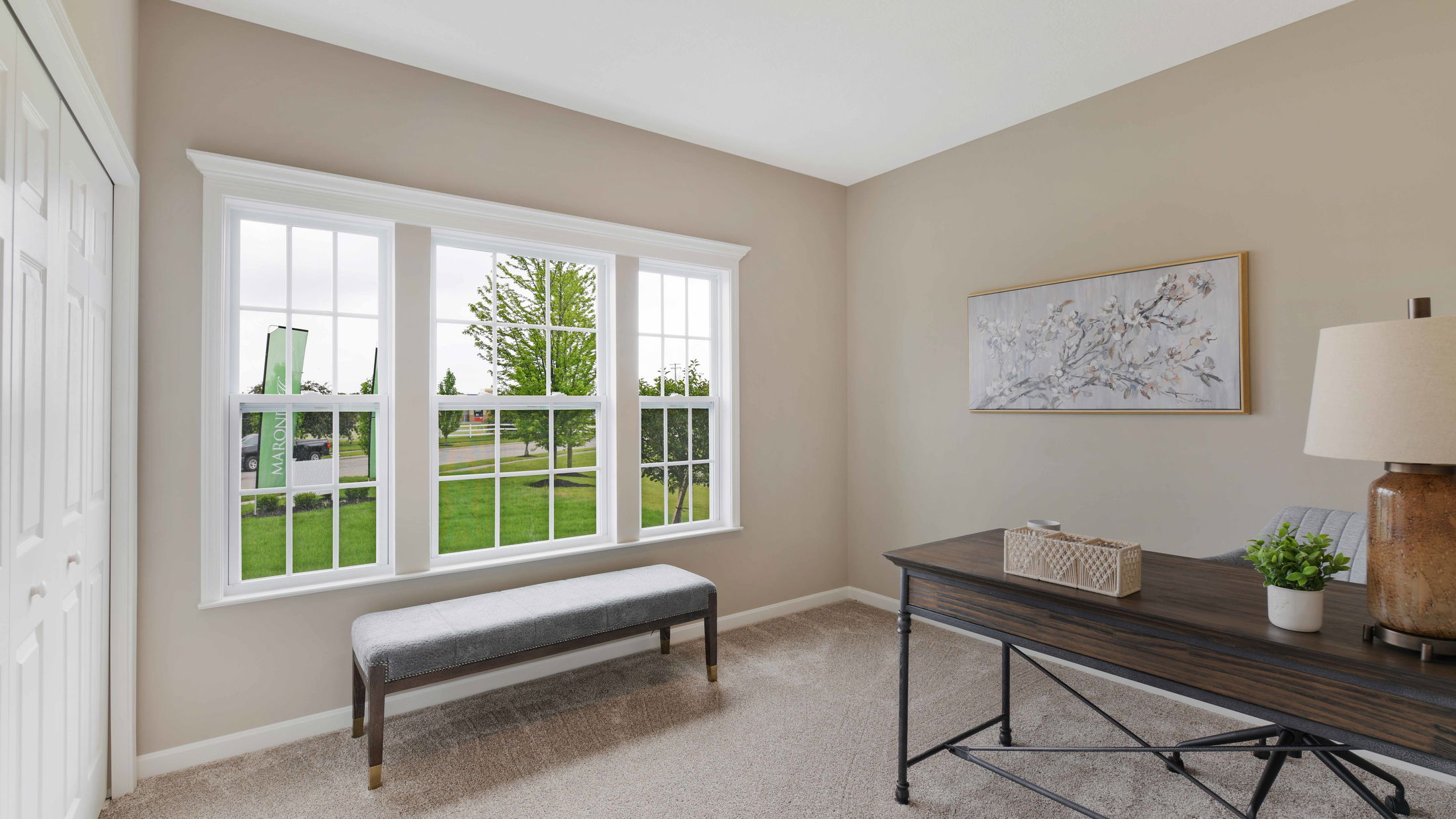 Bright home office with a large window, elegant wooden desk, and tasteful decor including a bench and wall art.