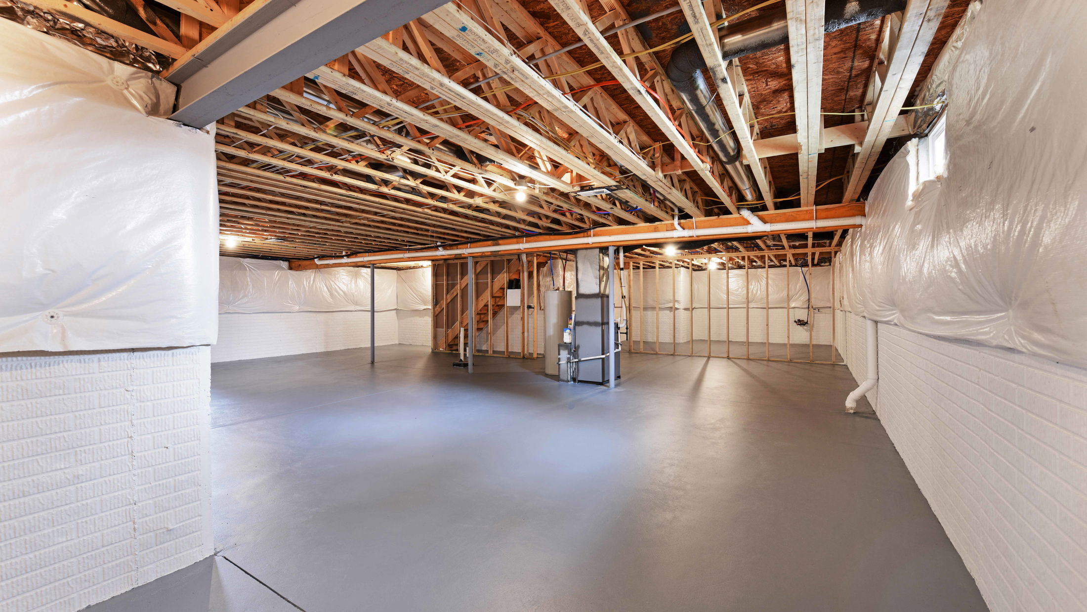 Modern unfinished basement with exposed beams, concrete floors, and partial insulation.