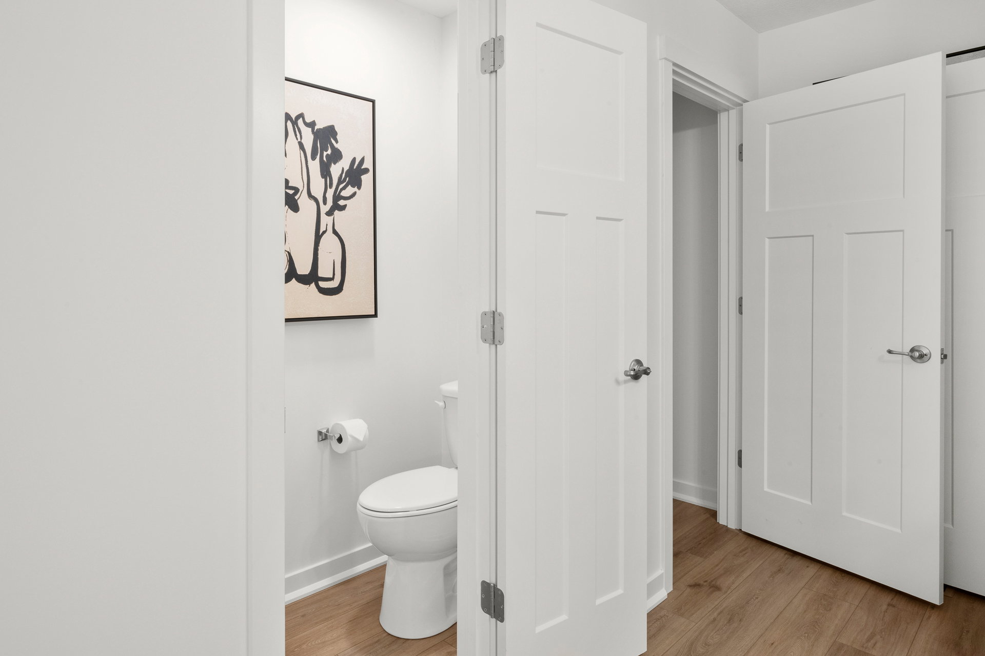 A modern bathroom with a toilet visible and two open doors leading to adjacent rooms.