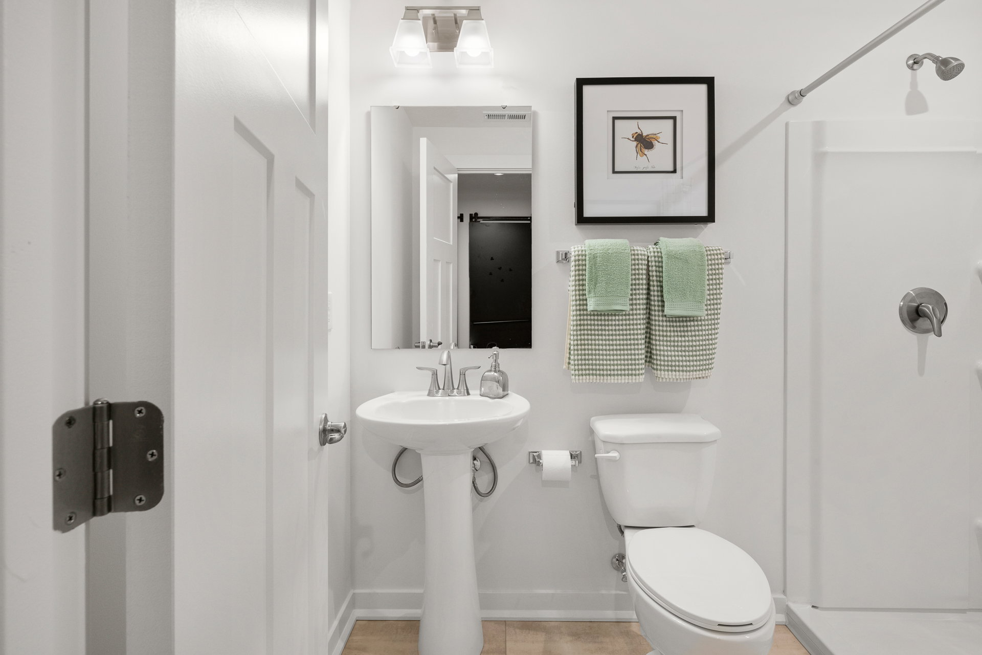 Modern bathroom featuring a white sink, toilet, and a shower, with green towels hanging and a framed print on the wall.