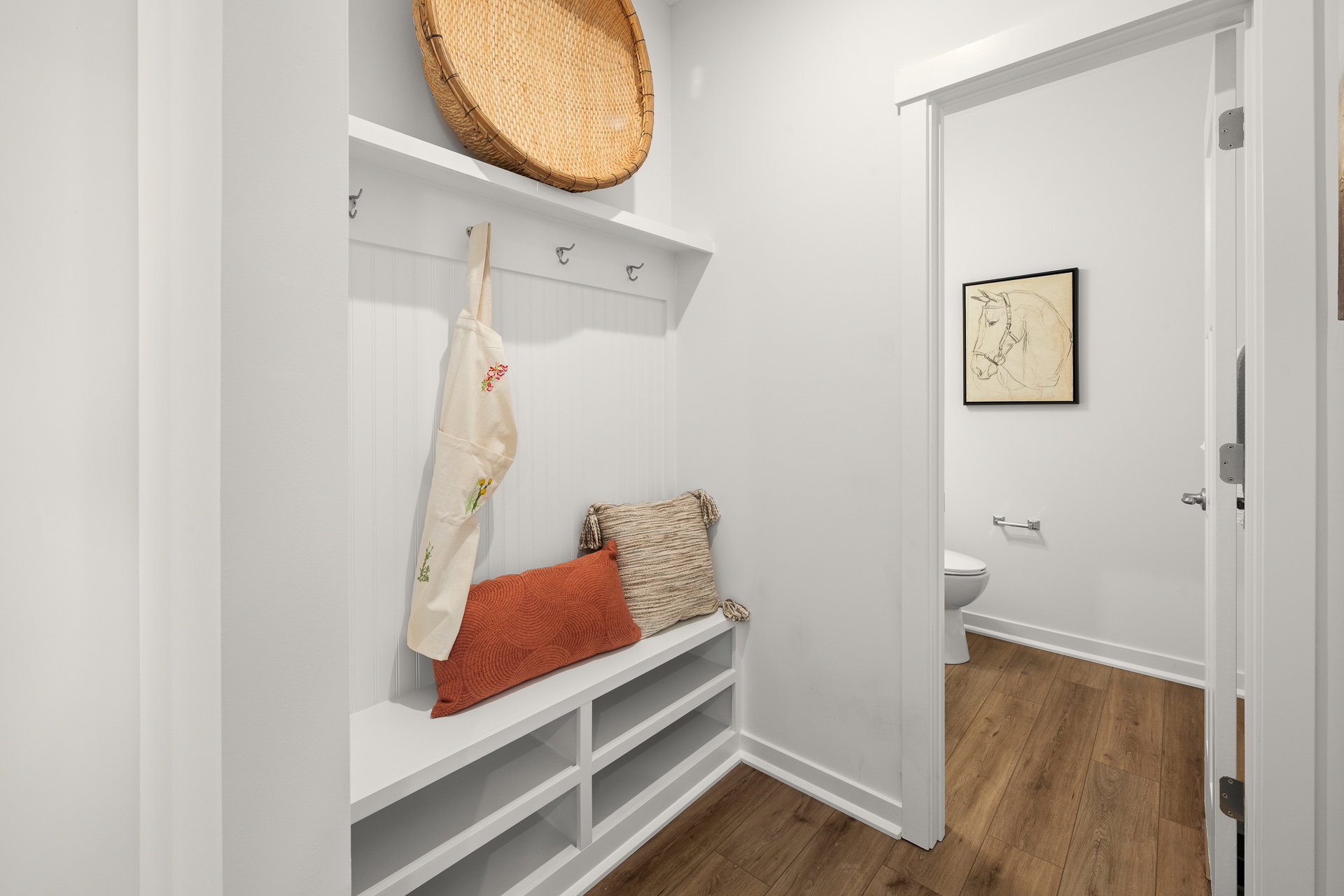 A modern entryway with a white bench, hooks, and decorative wall art.