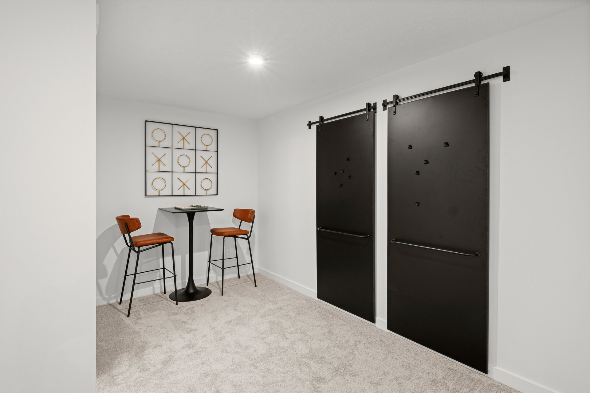 A small modern lounge area featuring two high stools, a round table, and a decorative wall with sliding black doors.