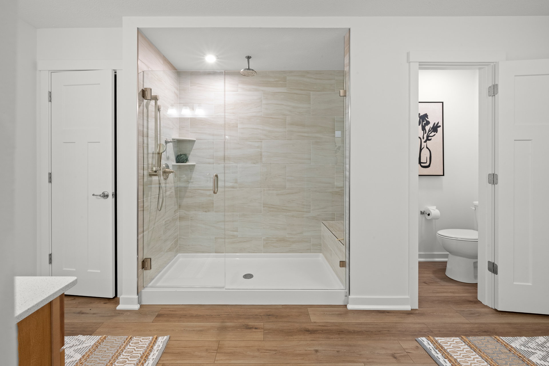Modern bathroom with a glass shower enclosure, tiled walls, and wooden flooring.