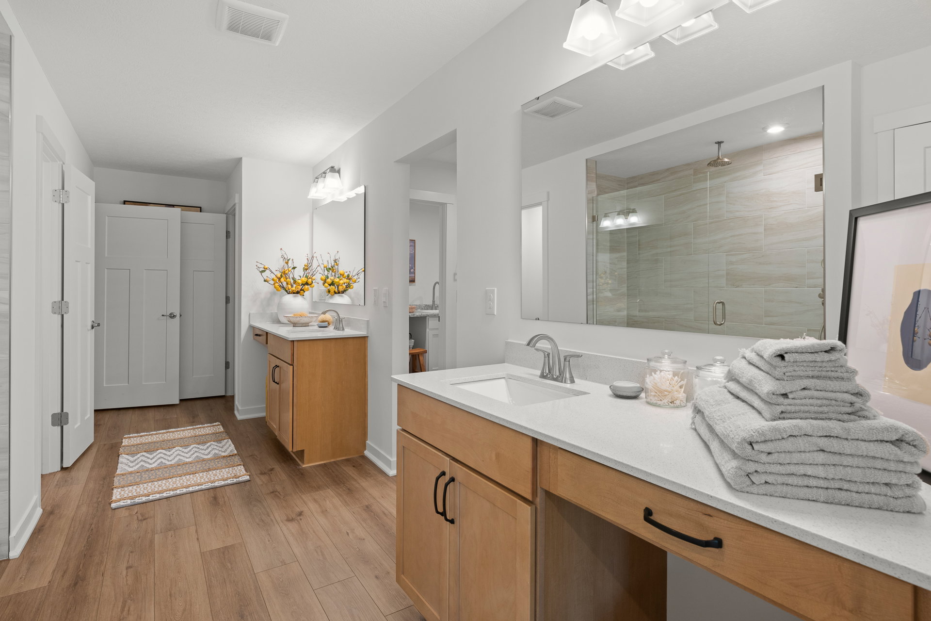 Bright modern bathroom featuring a large mirror, wooden cabinetry, neatly stacked towels, and a decorative plant.