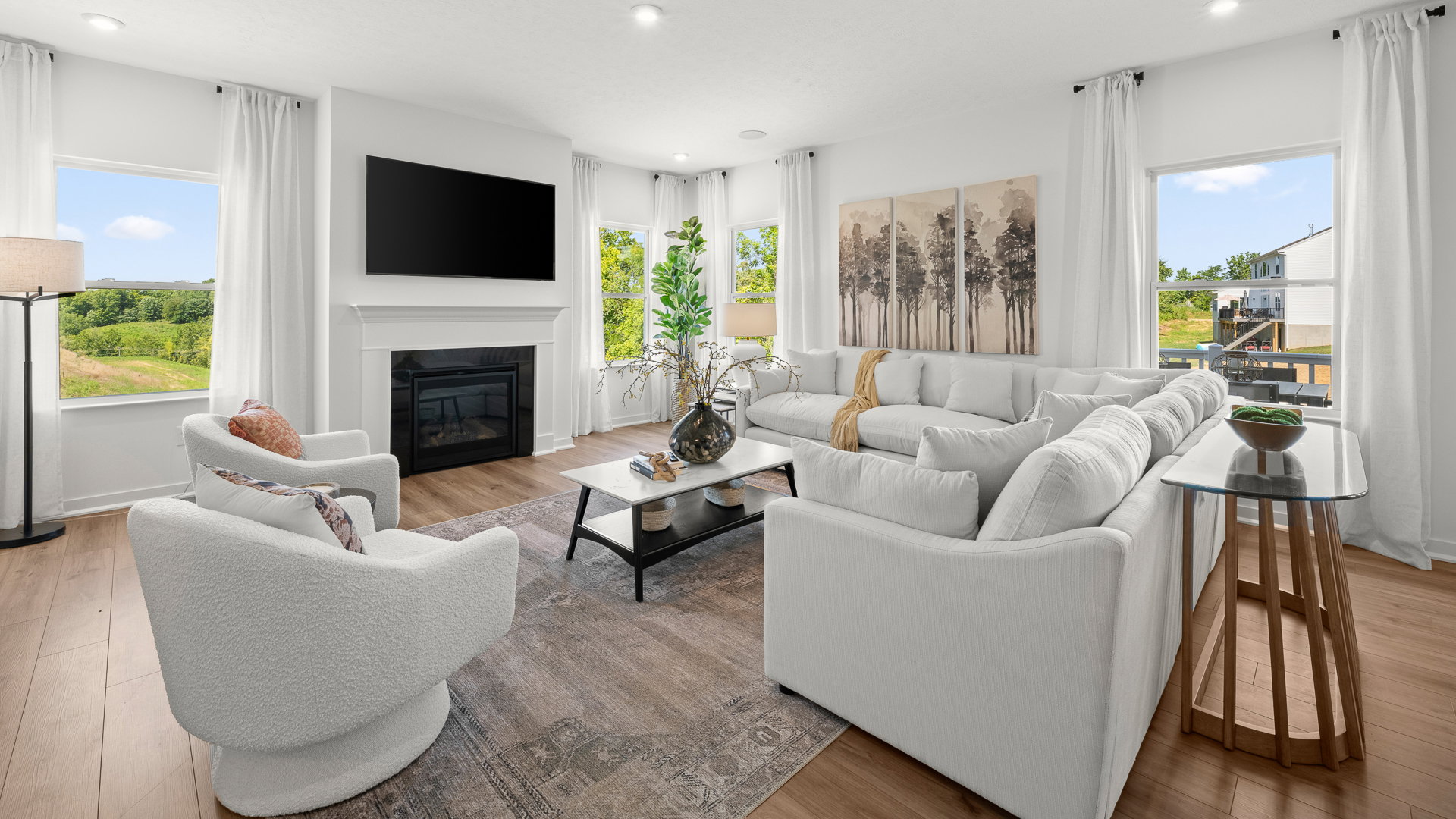 Bright and modern living room featuring a white sectional sofa, a fireplace, large windows, and decorative artwork.
