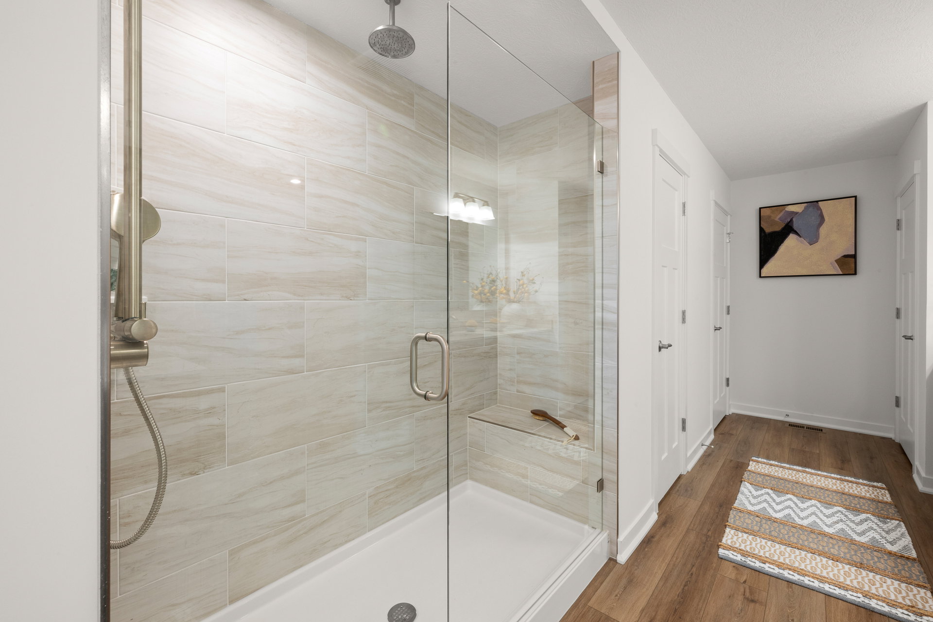 A modern bathroom featuring a glass shower with light-colored tiles and a decorative rug on the floor.
