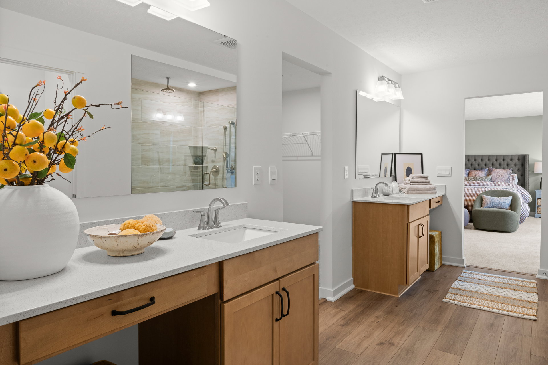 Modern bathroom featuring a double vanity with a bowl of lemons and a view into a bedroom with a bed and decorative pillows.
