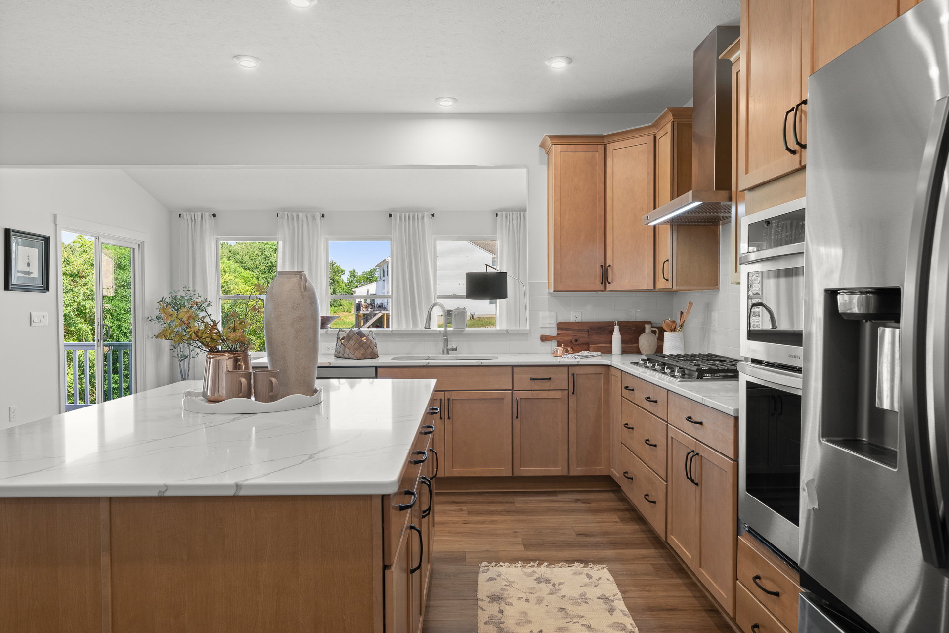 Modern kitchen featuring wooden cabinets, a large island with a white countertop, stainless steel appliances, and natural light streaming through the windows.