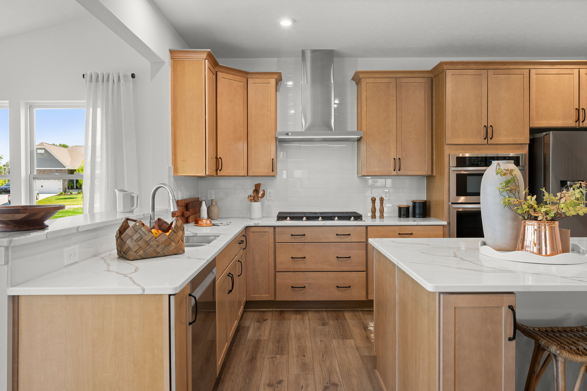 Modern kitchen with light wood cabinets, a marble countertop, a stainless steel stove, and a large window overlooking a garden.