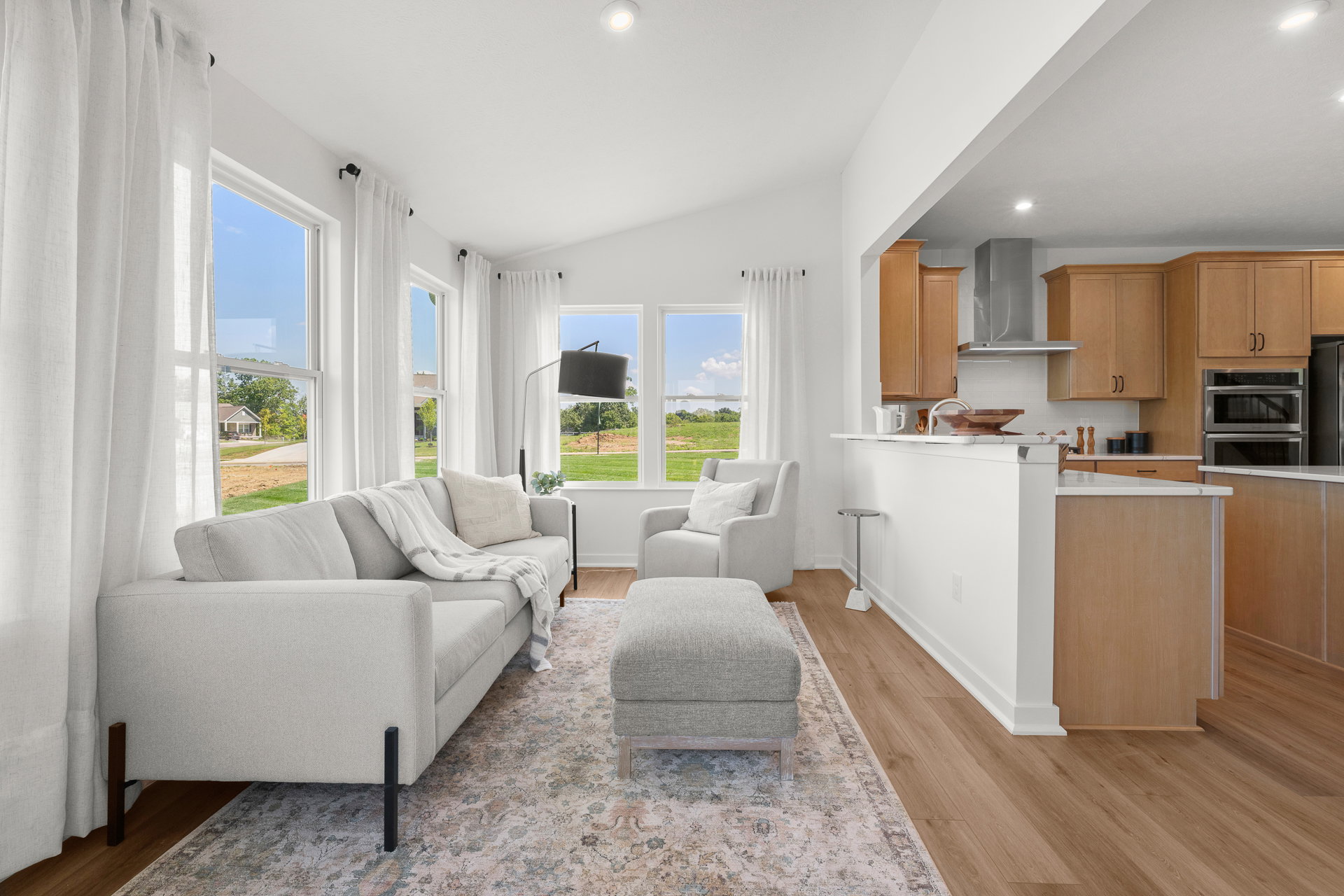 Bright, modern living room with a light gray sofa, armchairs, and a view of a green landscape through large windows.