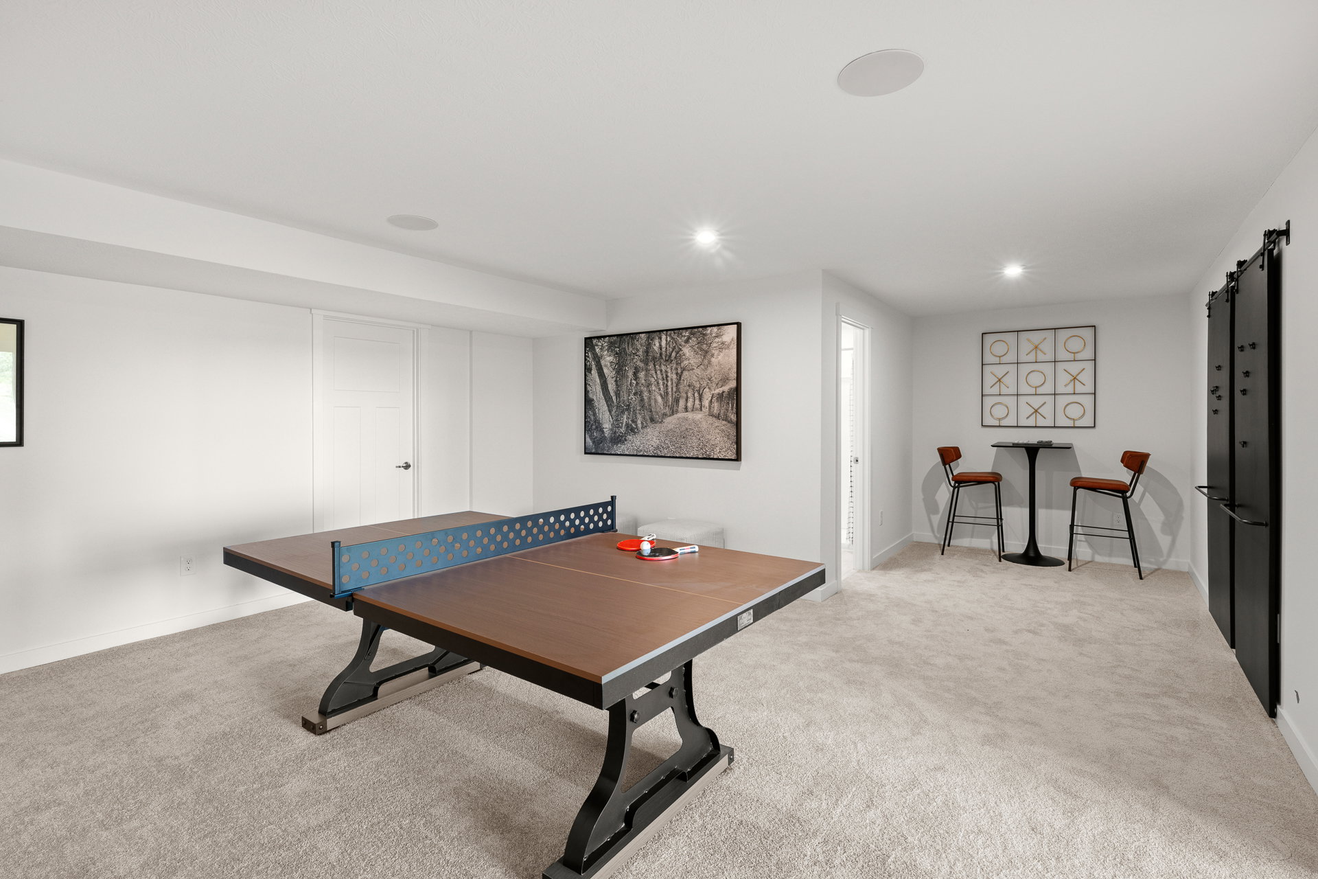 A modern game room with a ping pong table, accent chairs, and wall art in a light-colored setting.