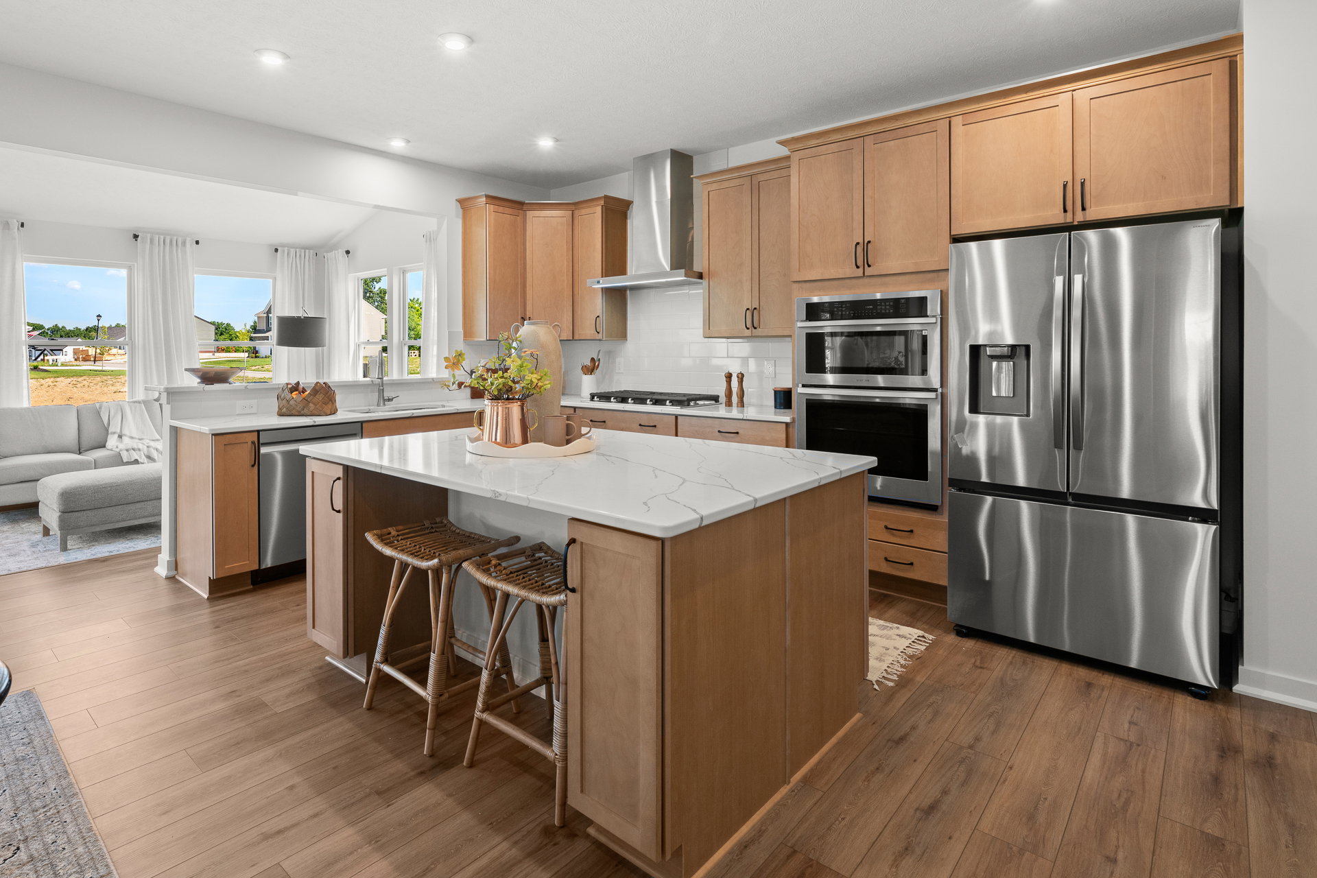 Modern kitchen featuring wooden cabinets, stainless steel appliances, a marble countertop island, and bar stools.