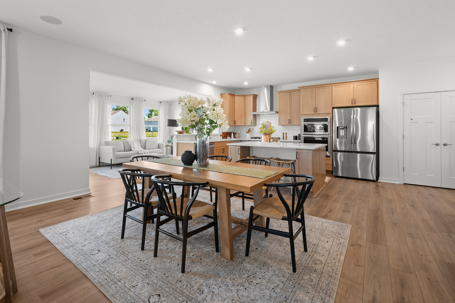 Bright, modern kitchen with a dining table, black chairs, and wooden cabinetry.