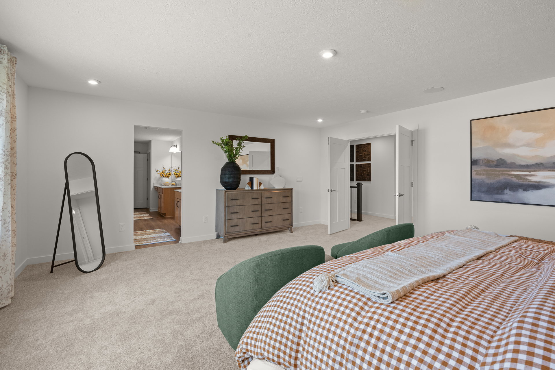 Brightly lit modern bedroom featuring a plaid bedspread, a large mirror, a dresser, and an abstract painting on the wall.