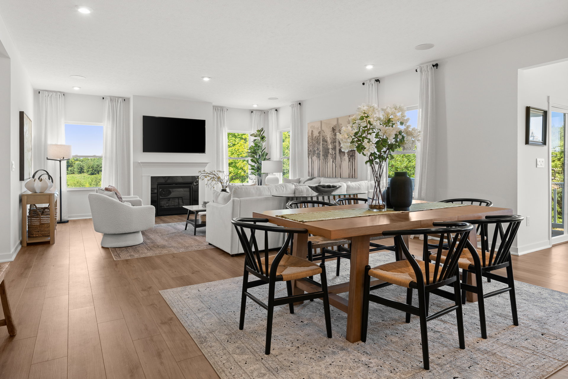 Bright living and dining area featuring a wooden table, black chairs, a cozy sofa, and large windows with scenic views.