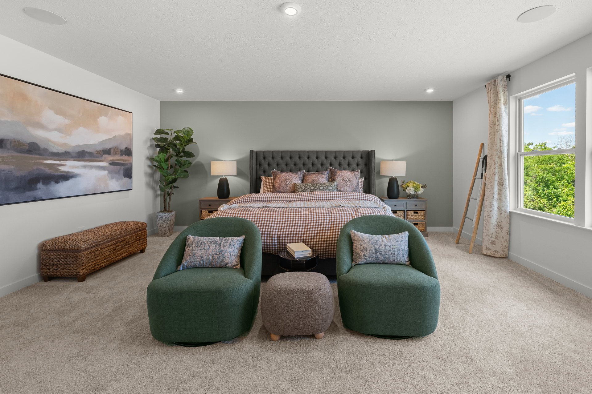 A modern bedroom featuring a gray upholstered bed, two green chairs, a small ottoman, and a large painting on the wall.