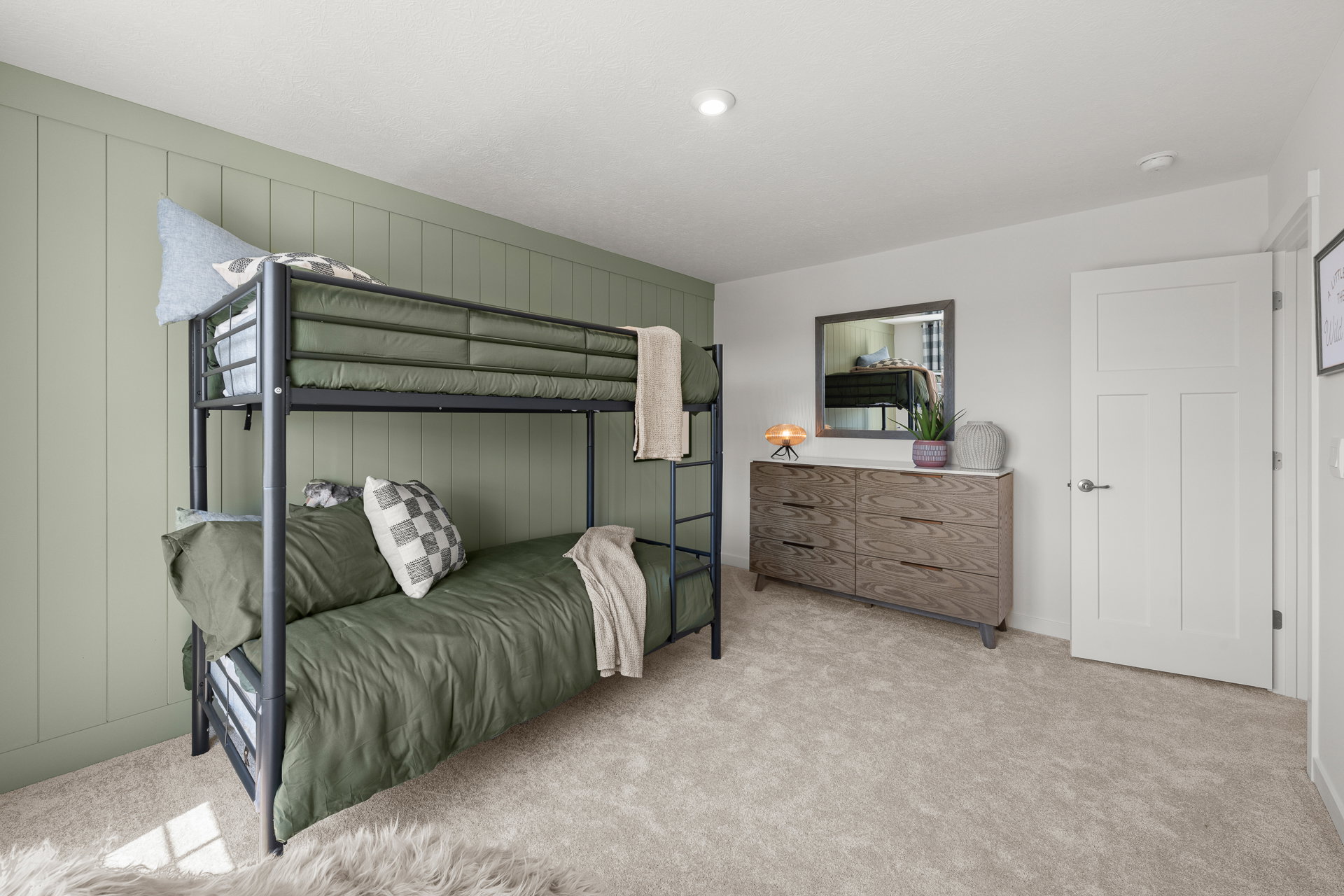 Bunk beds with green bedding and a dresser in a softly lit bedroom with green walls.