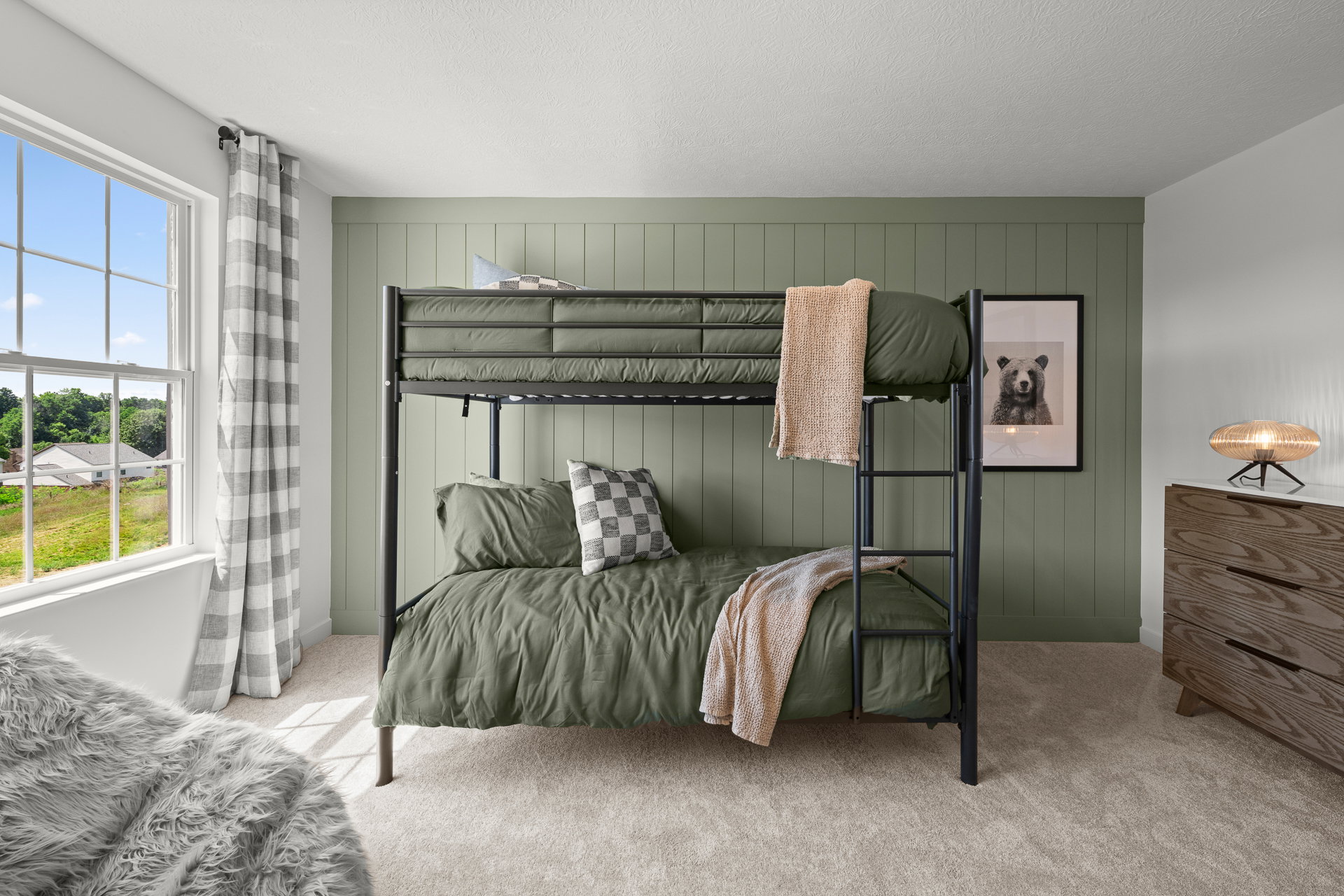 A modern bedroom featuring a black bunk bed with green bedding, a decorative throw, and a large window with a scenic view.