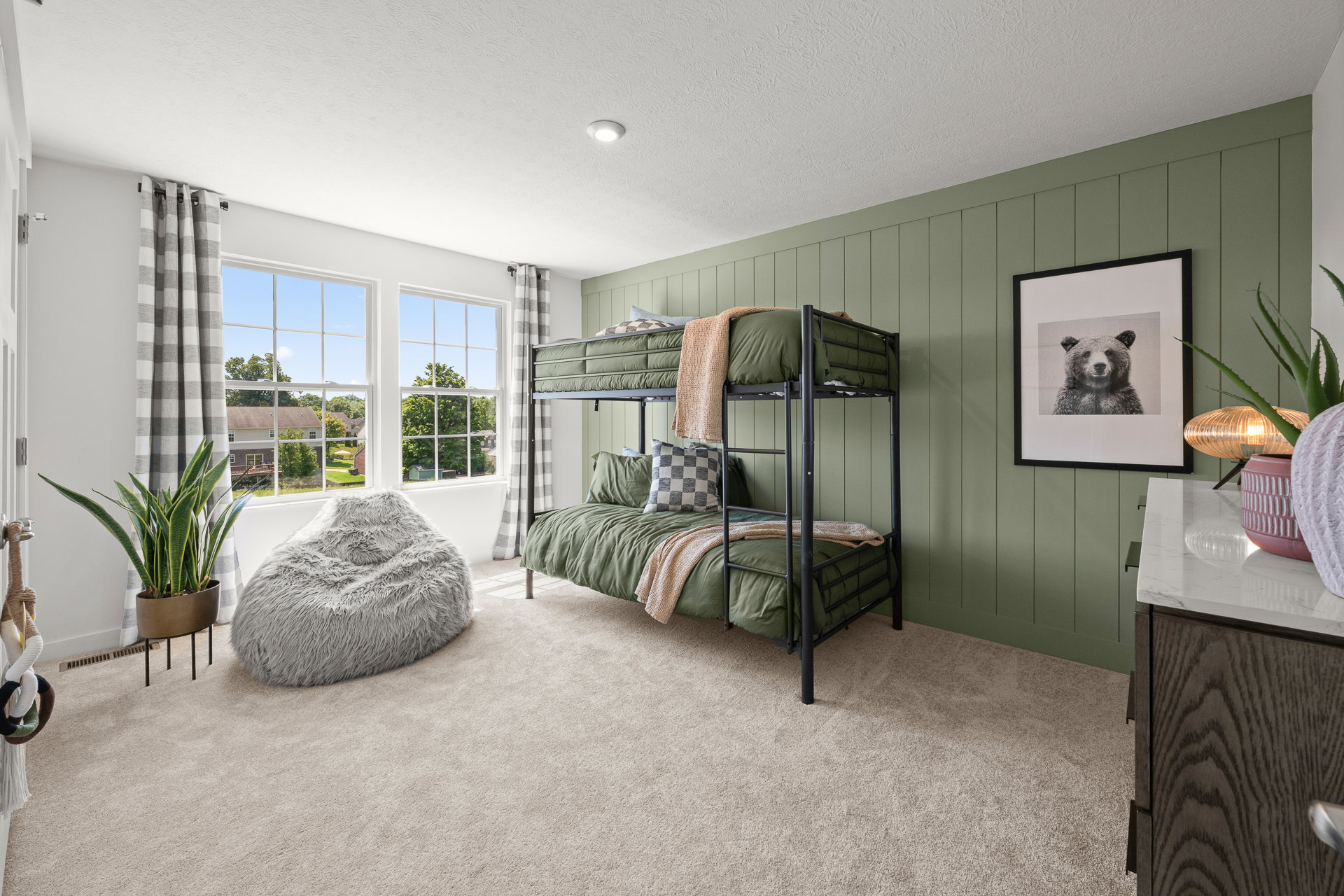 A cozy bedroom featuring a bunk bed with green bedding, a bean bag chair, a panda print on the wall, and large windows letting in natural light.
