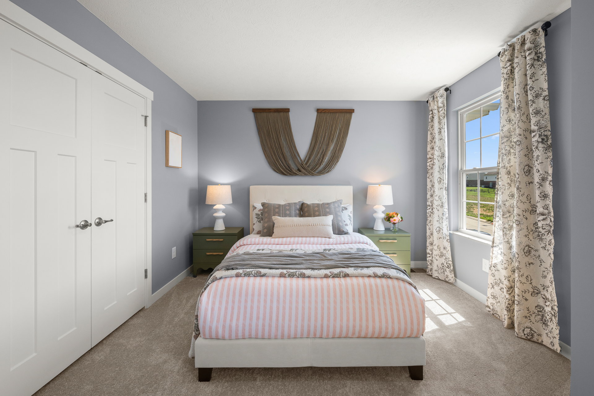 A cozy bedroom featuring a white bed with striped bedding, decorative pillows, bedside tables, and large windows with patterned curtains.