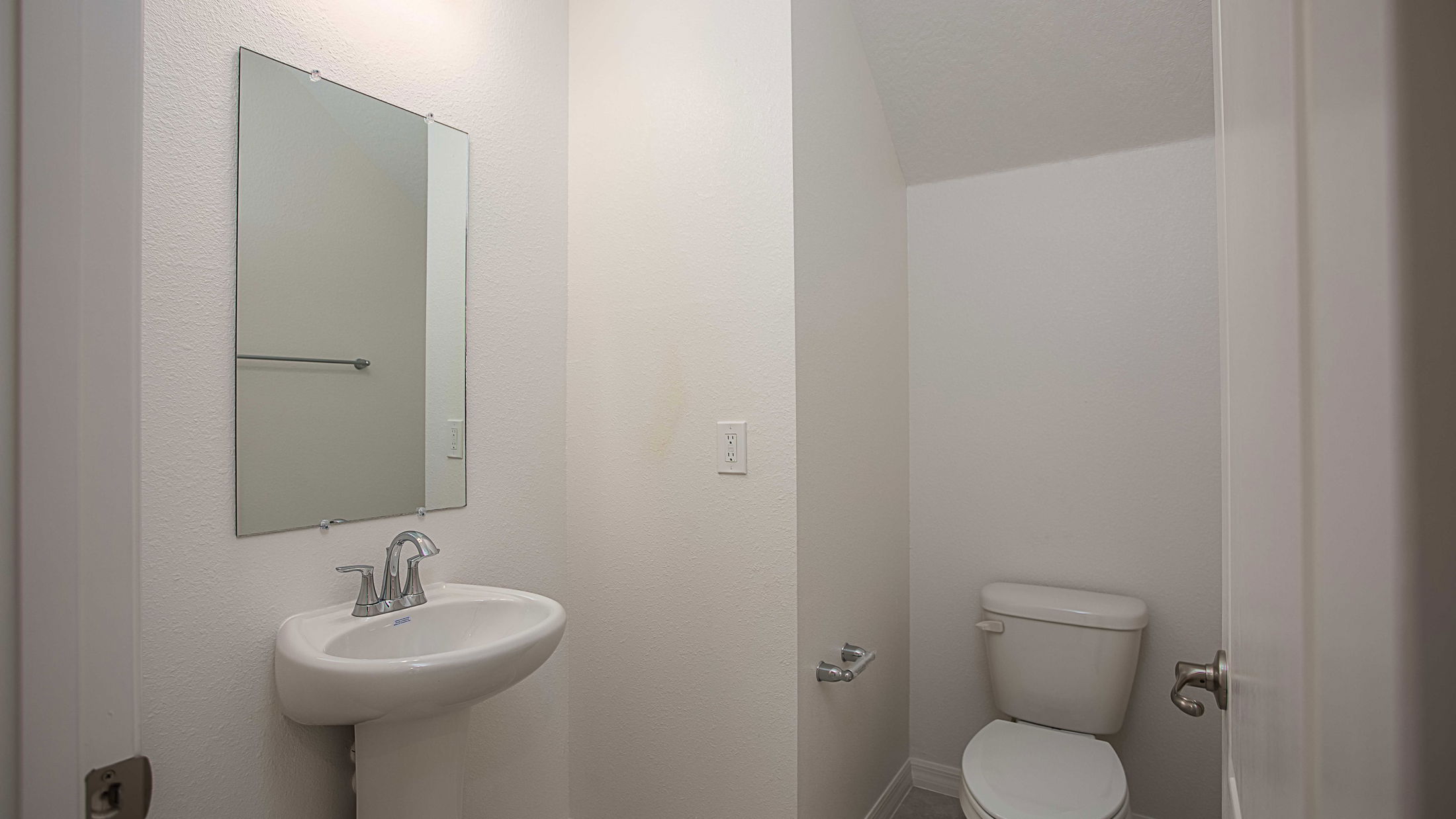 Compact bathroom with a white sink, mirror, and toilet in a minimalist white-tiled space.