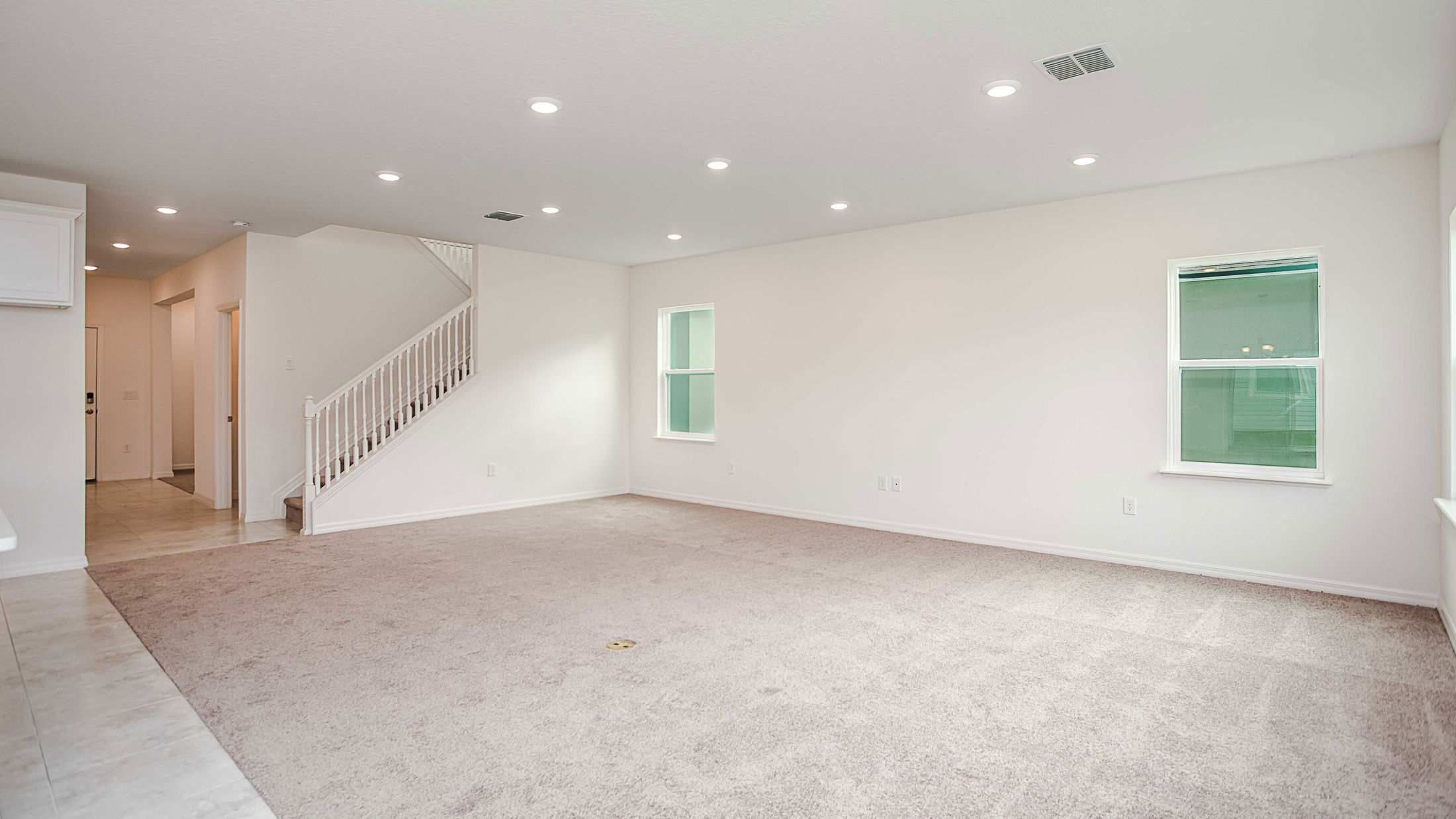 Spacious, well-lit empty living room with beige carpet, white walls, and staircase in a modern home.