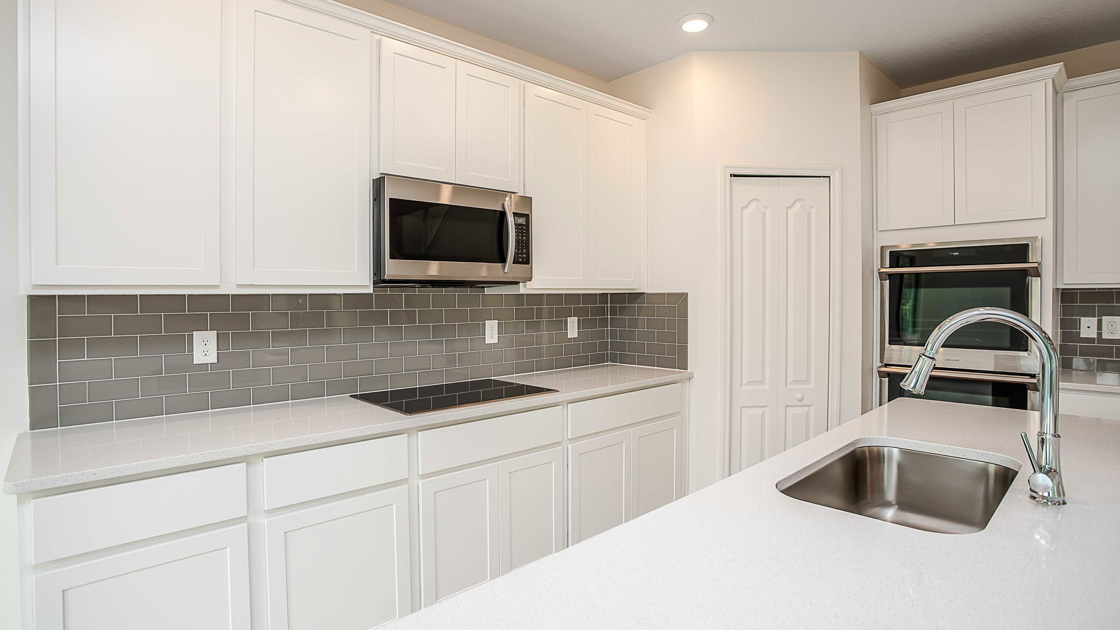 Modern kitchen with white cabinets, stainless steel appliances, and a sleek gray subway tile backsplash.