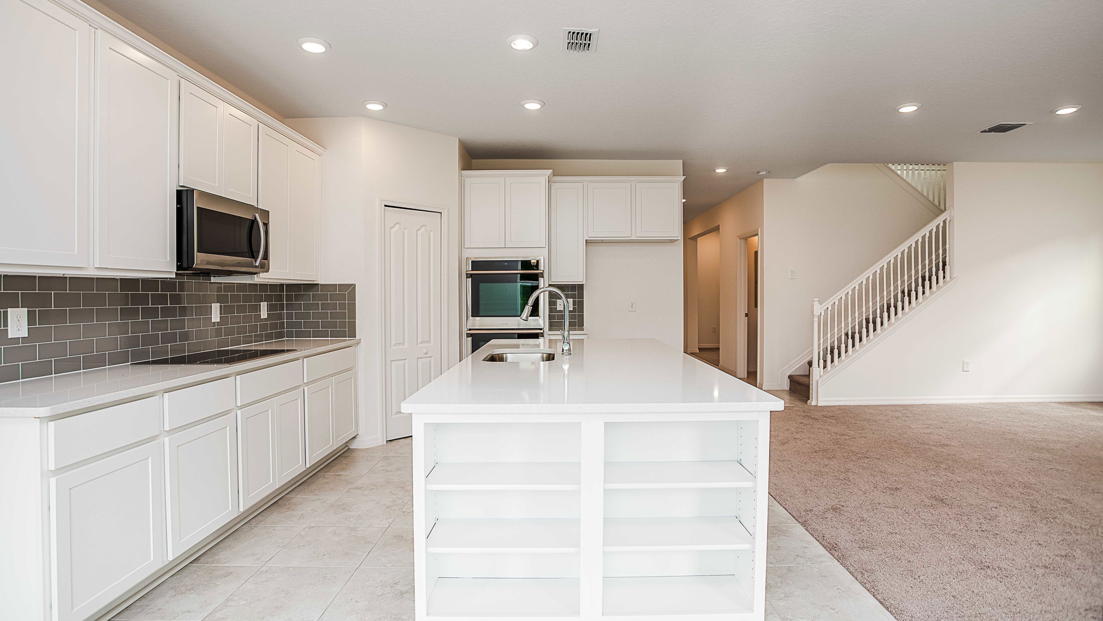 Modern kitchen with white cabinets, a central island, stainless steel appliances, and a gray tile backsplash in a spacious open-concept home.