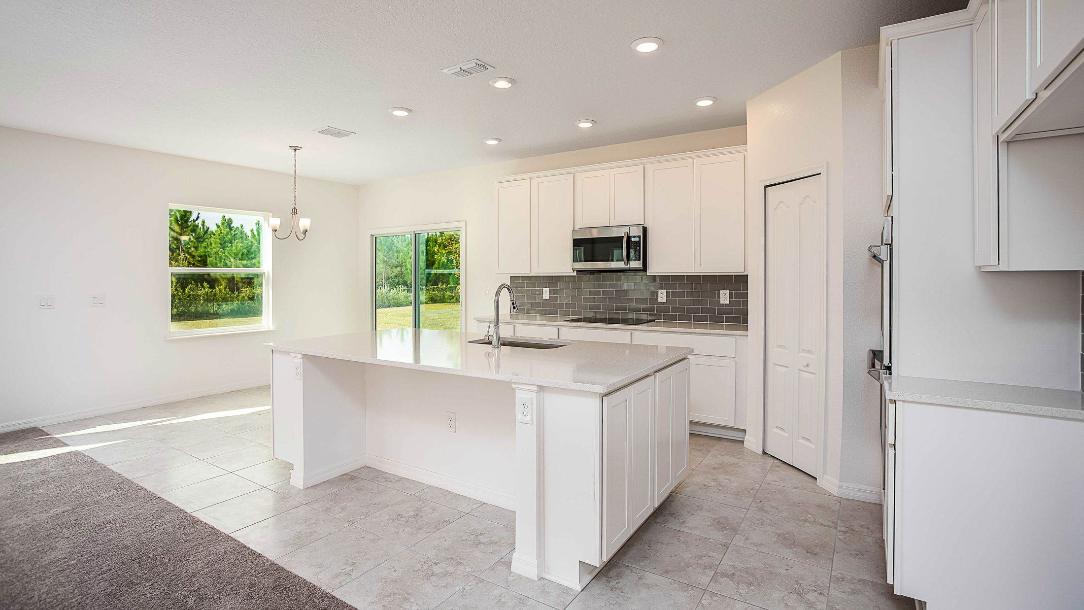 Modern, sunlit kitchen with white cabinetry, quartz countertops, and a stainless steel oven, overlooking a green outdoor view.