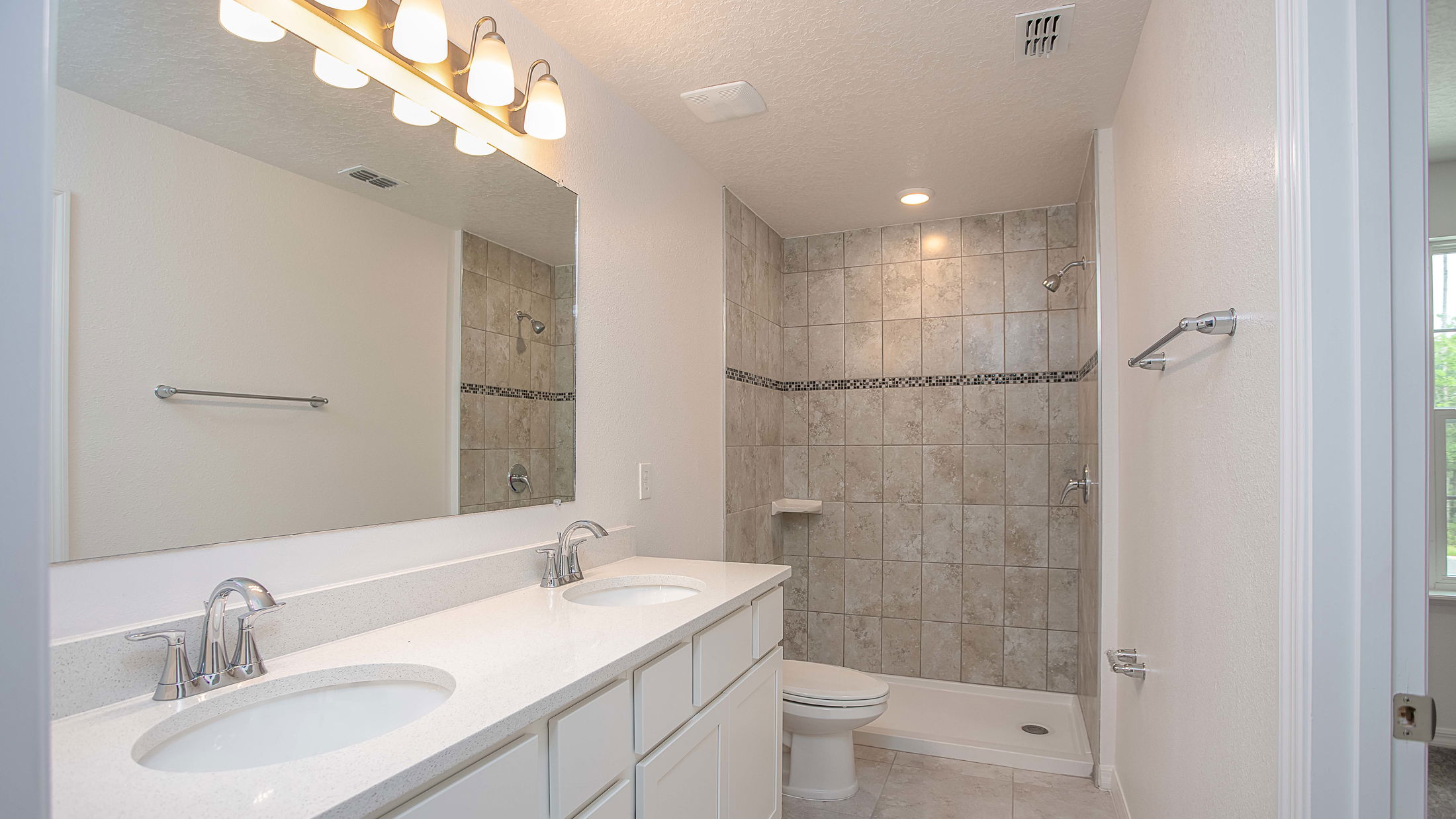 Modern bathroom with dual sinks, a large mirror, and a tiled walk-in shower.