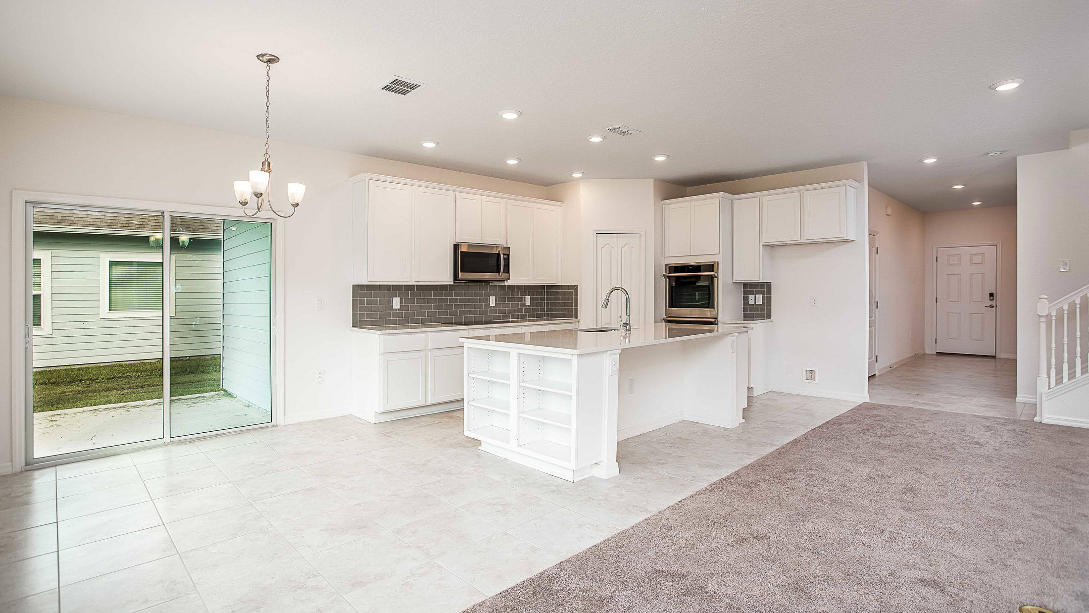 Modern kitchen and living area with white cabinets, gray tile backsplash, and sliding glass doors leading to a patio.