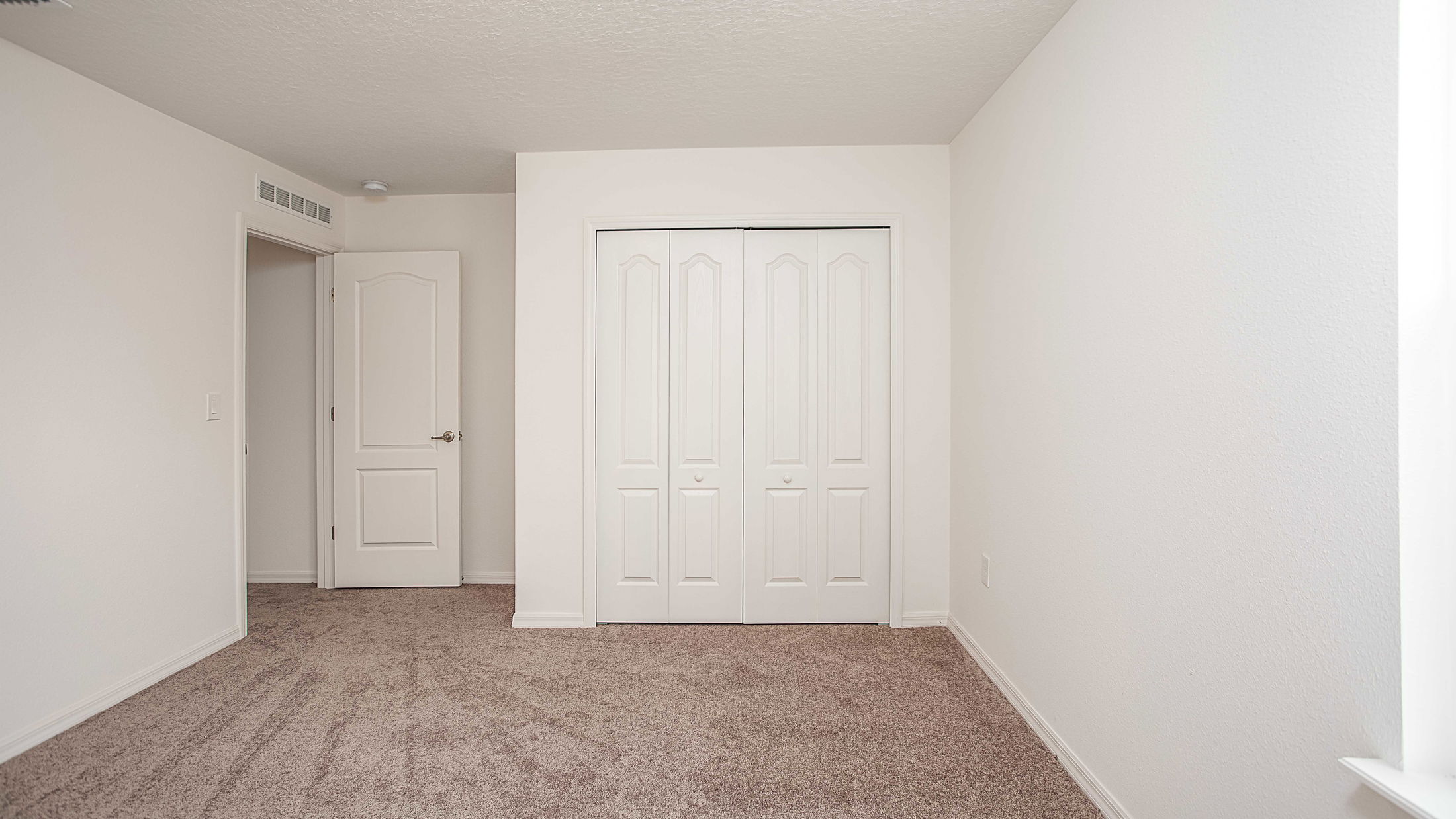 Empty bedroom with beige carpet, white walls, and a closed double closet door.