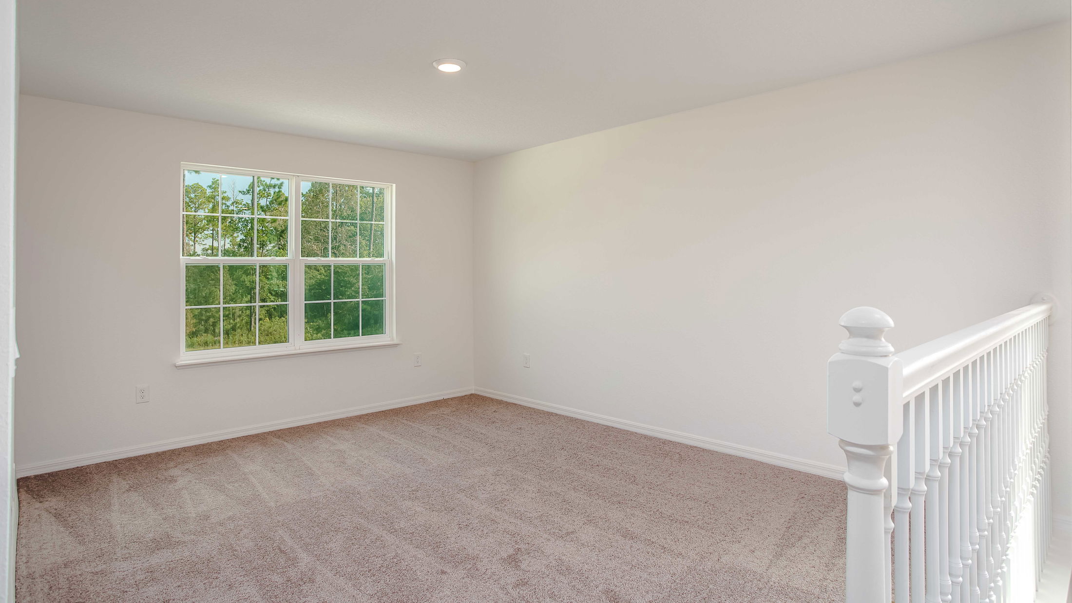 Bright, unfurnished room with beige carpet, large window, and white railing, showcasing natural light and a minimalist interior design.