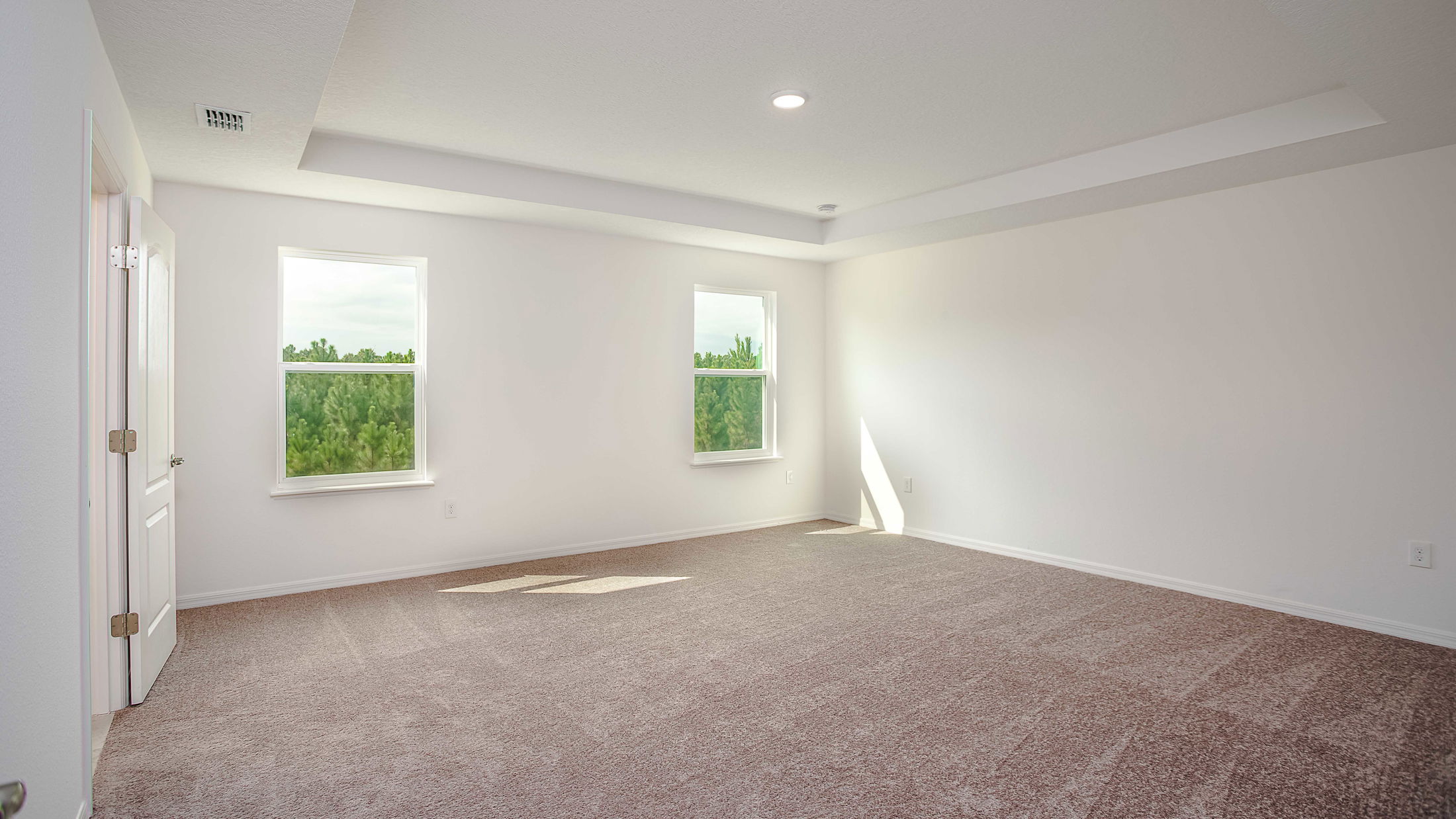 Bright, empty room with carpet flooring, two windows, and white walls.