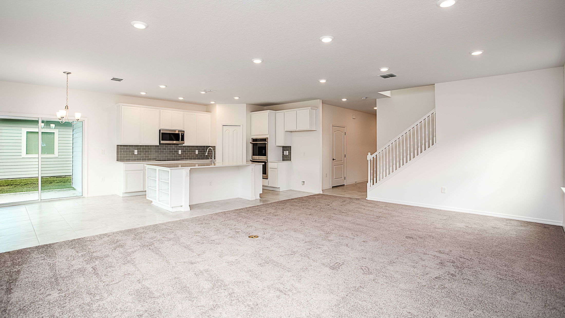 Spacious open-concept living area with carpeted floor, modern kitchen, and sliding glass doors in a bright, newly constructed home.