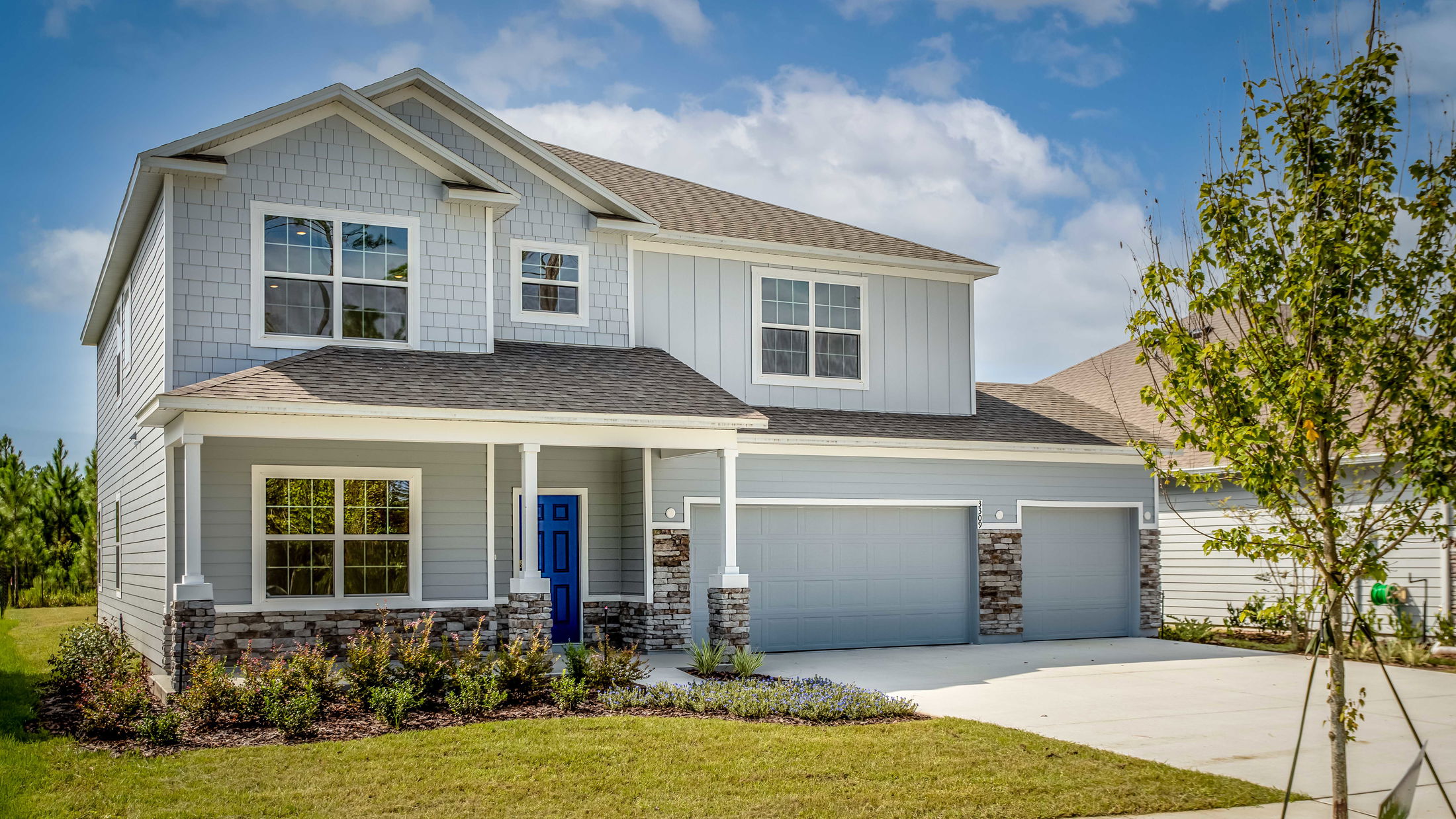 Modern two-story grey house with a blue front door, double garage, and landscaped yard.