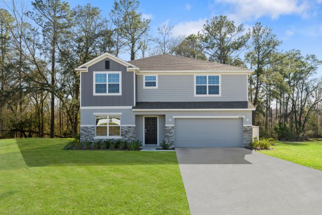 Modern two-story gray house with a spacious lawn and a driveway, surrounded by tall trees.