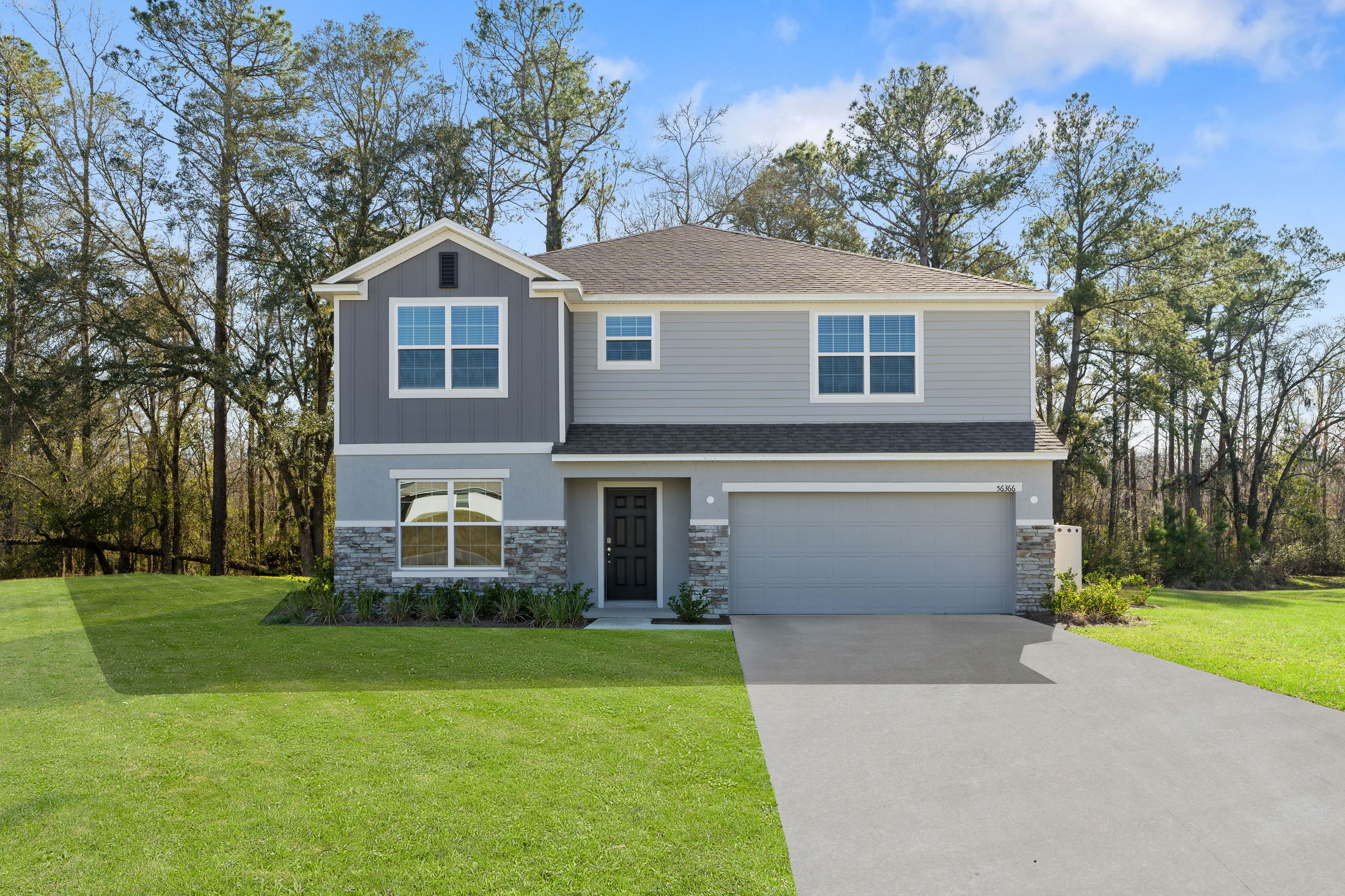Modern two-story gray house with a manicured front lawn and attached garage in a wooded area.