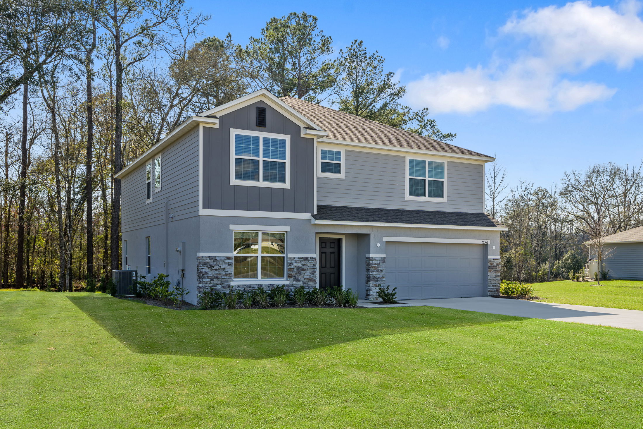 Modern two-story gray house with a manicured lawn and attached garage in a suburban setting.