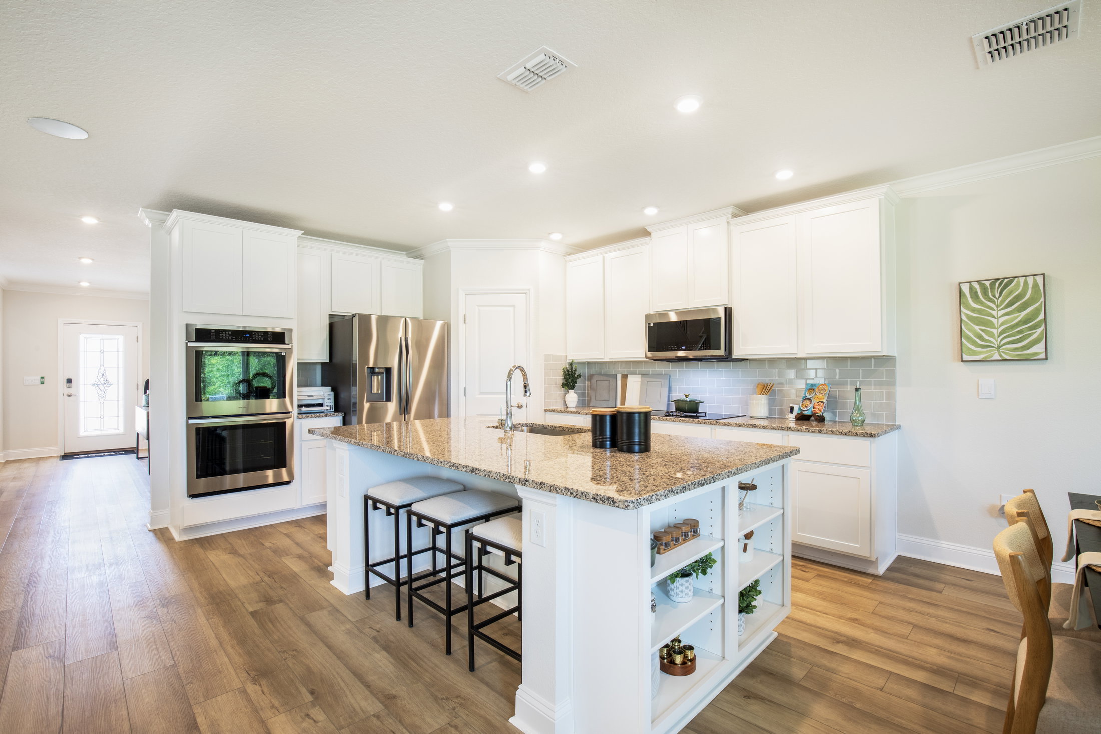 Modern kitchen with a large granite island, stainless steel appliances, and white cabinetry.