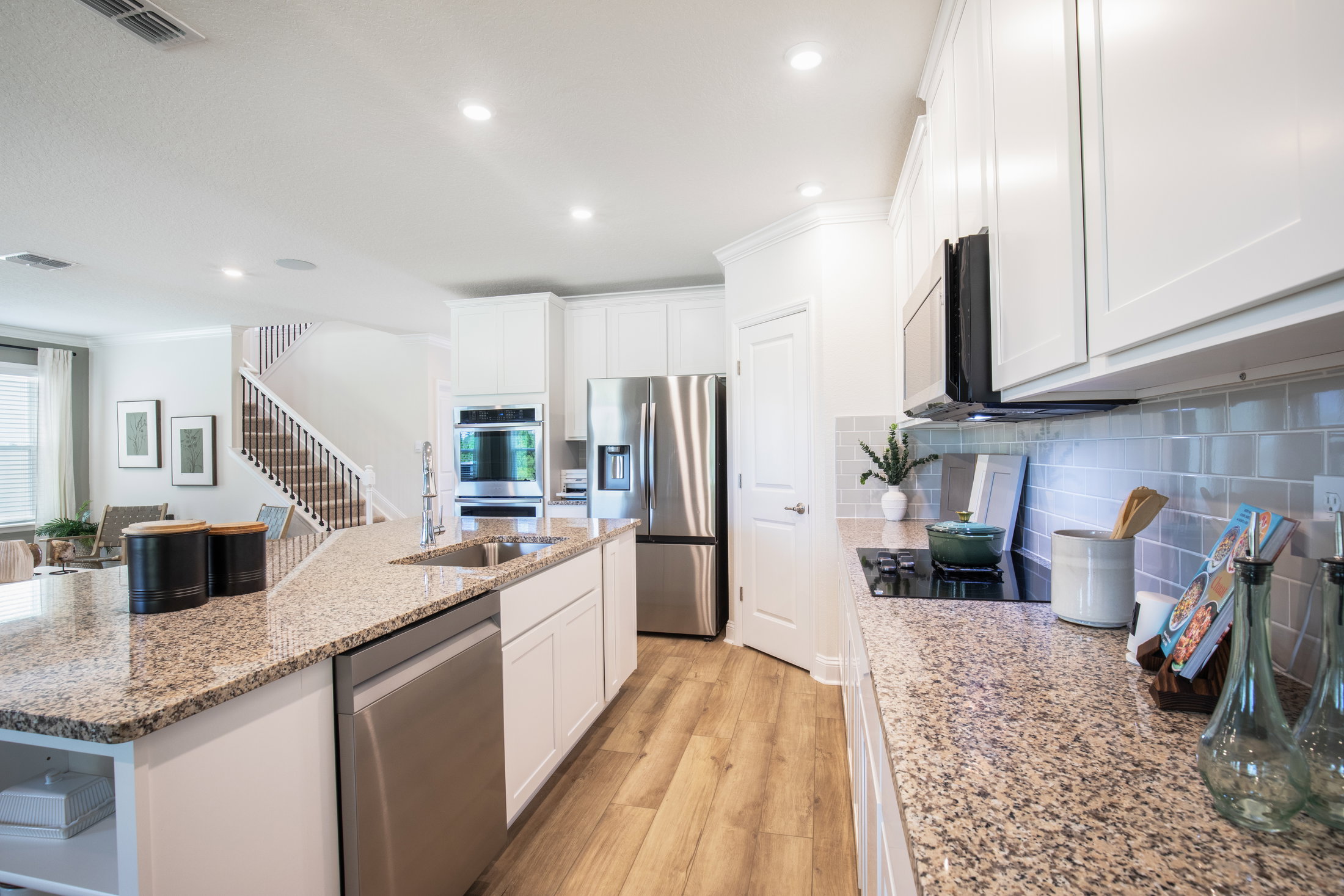 Modern kitchen featuring granite countertops, white cabinetry, stainless steel appliances, and hardwood flooring.