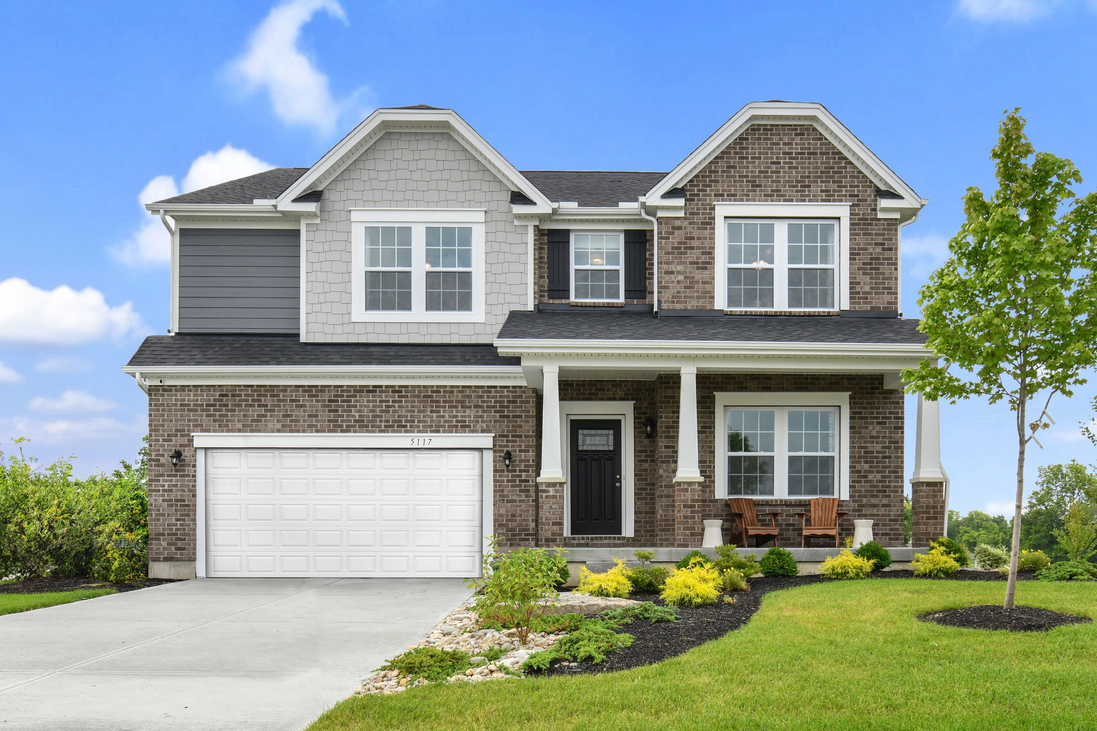 Two-story modern brick house with white garage and manicured lawn under a clear blue sky.